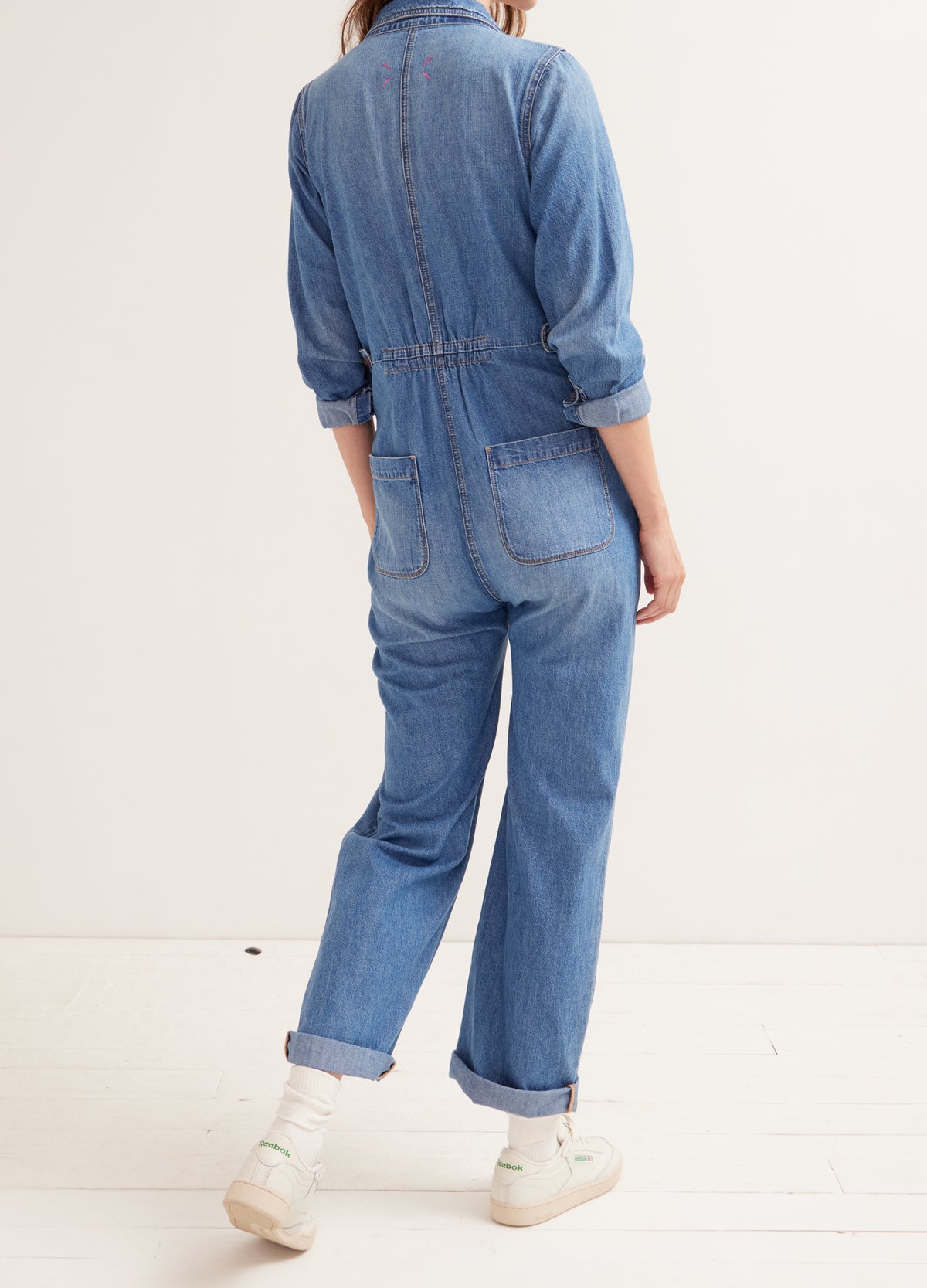 Indigo denim maternity jumpsuit with rolled cuffs and elasticized waist, worn by pregnant model from back.