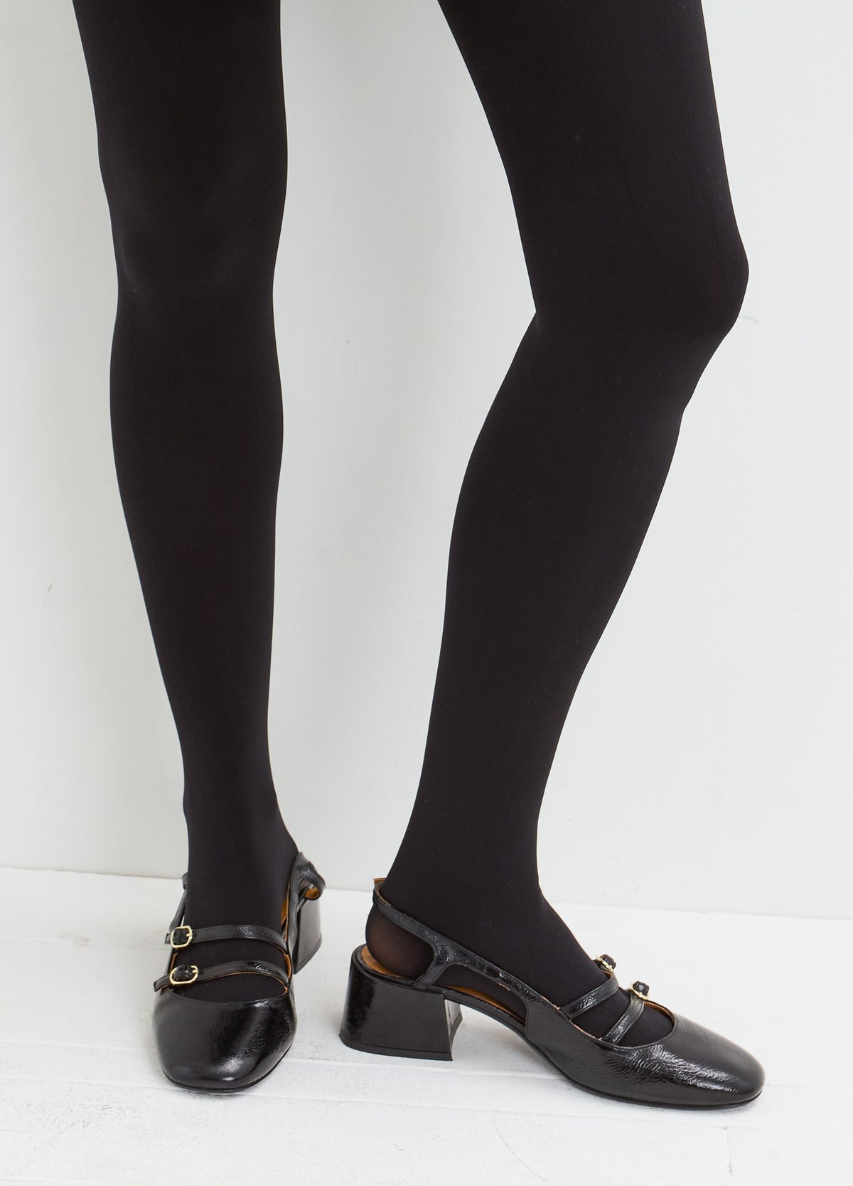 Sheer black tights on legs, paired with black leather loafers with gold-tone chain detailing.