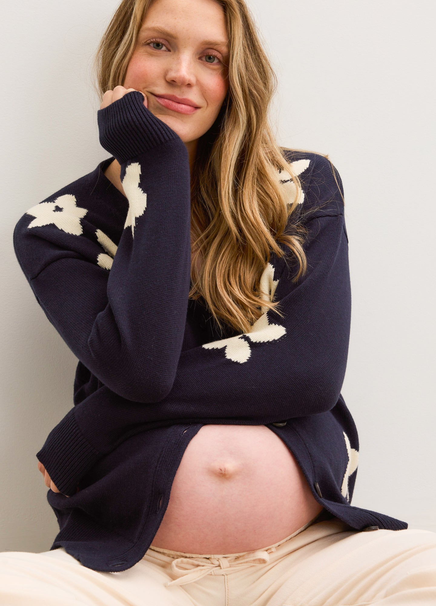 Navy oversized cardigan with white floral jacquard pattern, worn open over maternity beige pants.