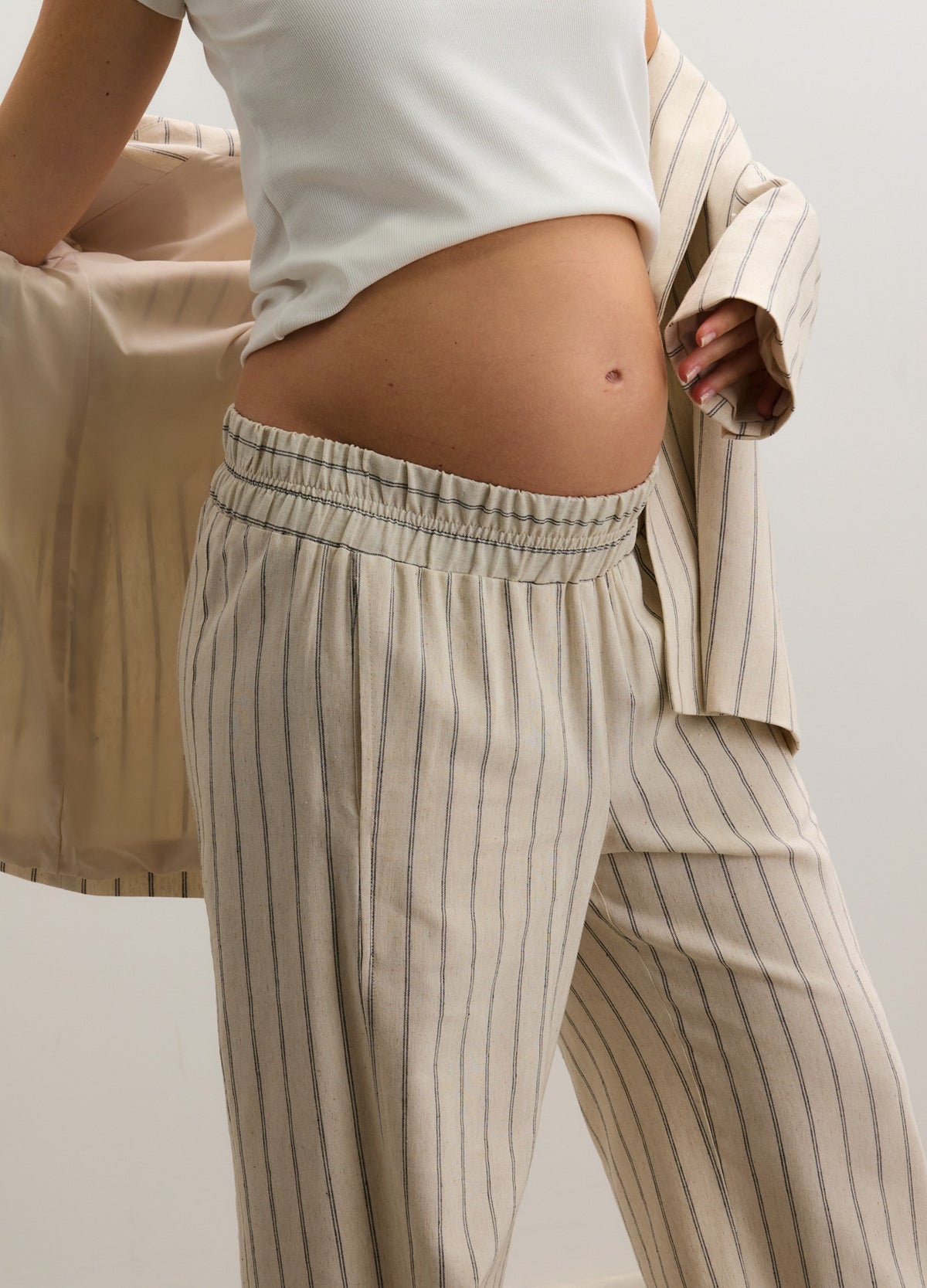 Beige maternity pants with thin vertical stripes, elastic waistband designed for pregnant belly comfort.
