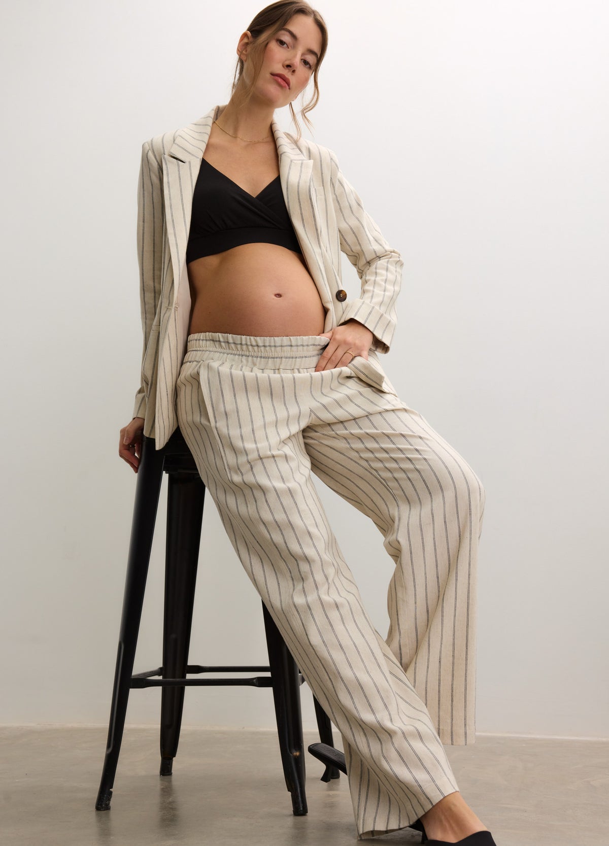 White pinstripe maternity pants with a relaxed fit and elastic waistband paired with a black crop top and light striped.