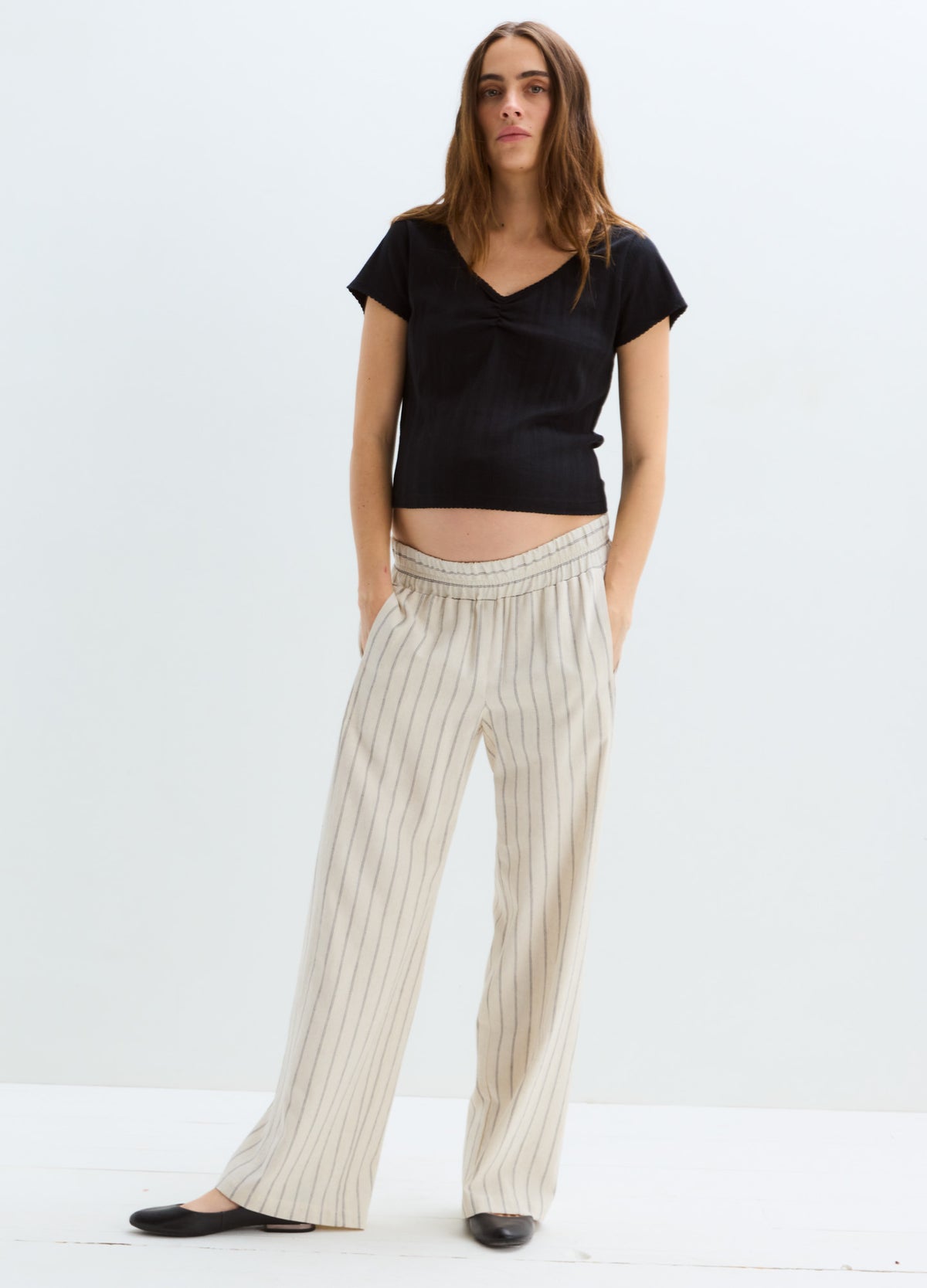 Beige and white vertical striped maternity pants with a relaxed wide-leg fit and a soft waistband, styled with a black.