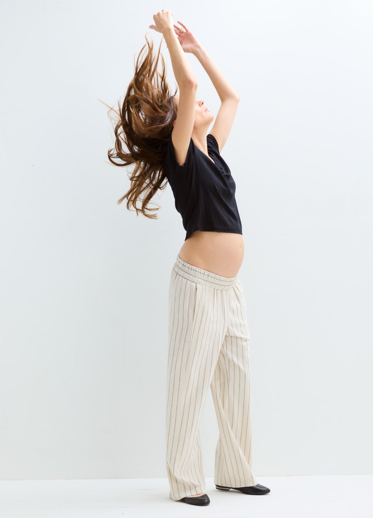 Light beige maternity pants with vertical pinstripes and a relaxed wide-leg fit worn by a pregnant woman.