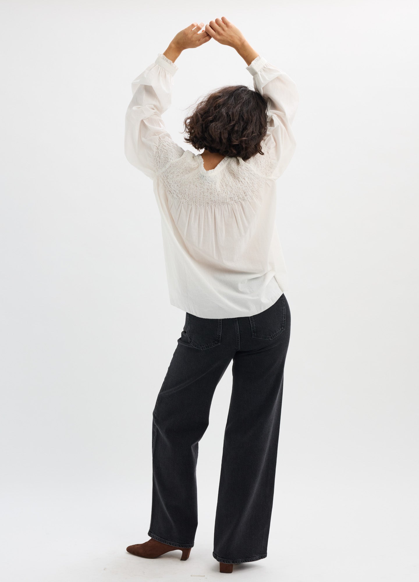 White loose maternity blouse with billowy long sleeves and gathered yoke detail worn with black wide-leg pants.