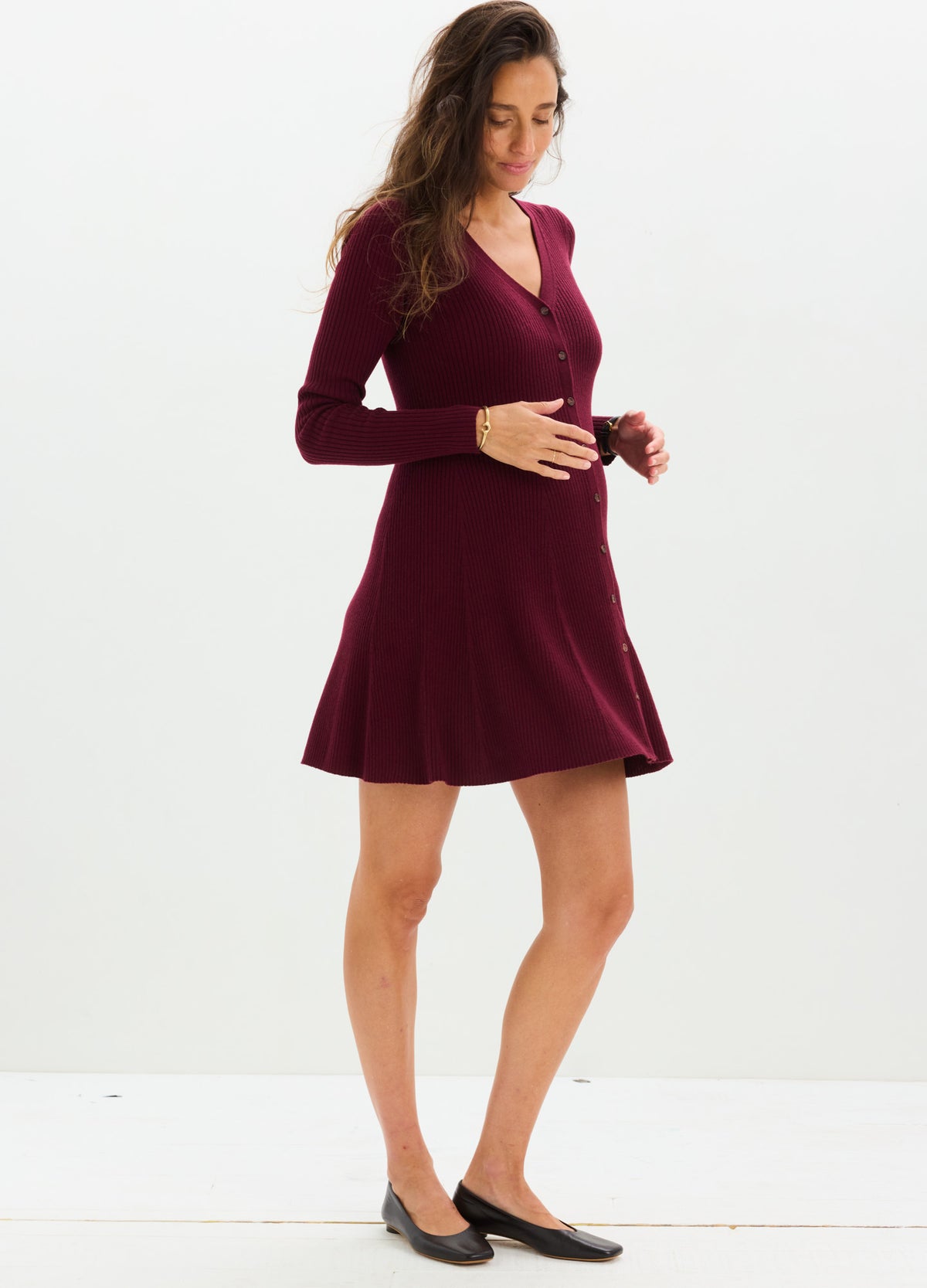 Burgundy knit mini sweater dress with long sleeves and V-neck, styled for maternity with a fitted waist and flare hem.