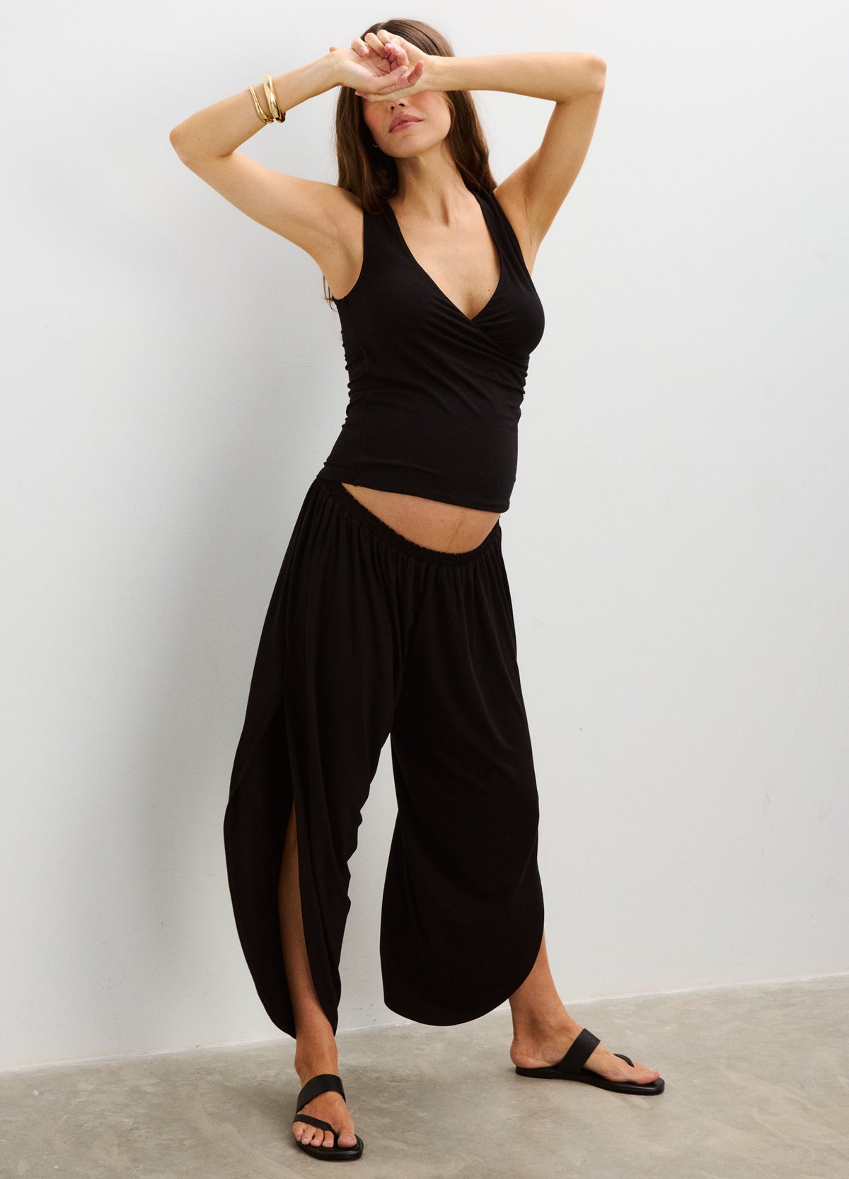 Black maternity pants with wide legs and high, stretchy waistband designed for pregnant bellies, worn with a black tank top.