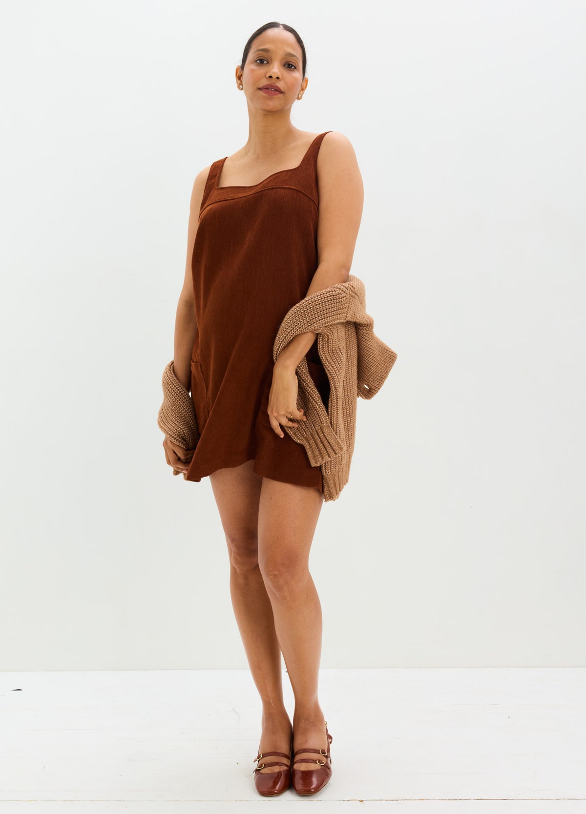 Brown corduroy mini dress with spaghetti straps, designed for maternity, paired with matching knit cardigan and heels.