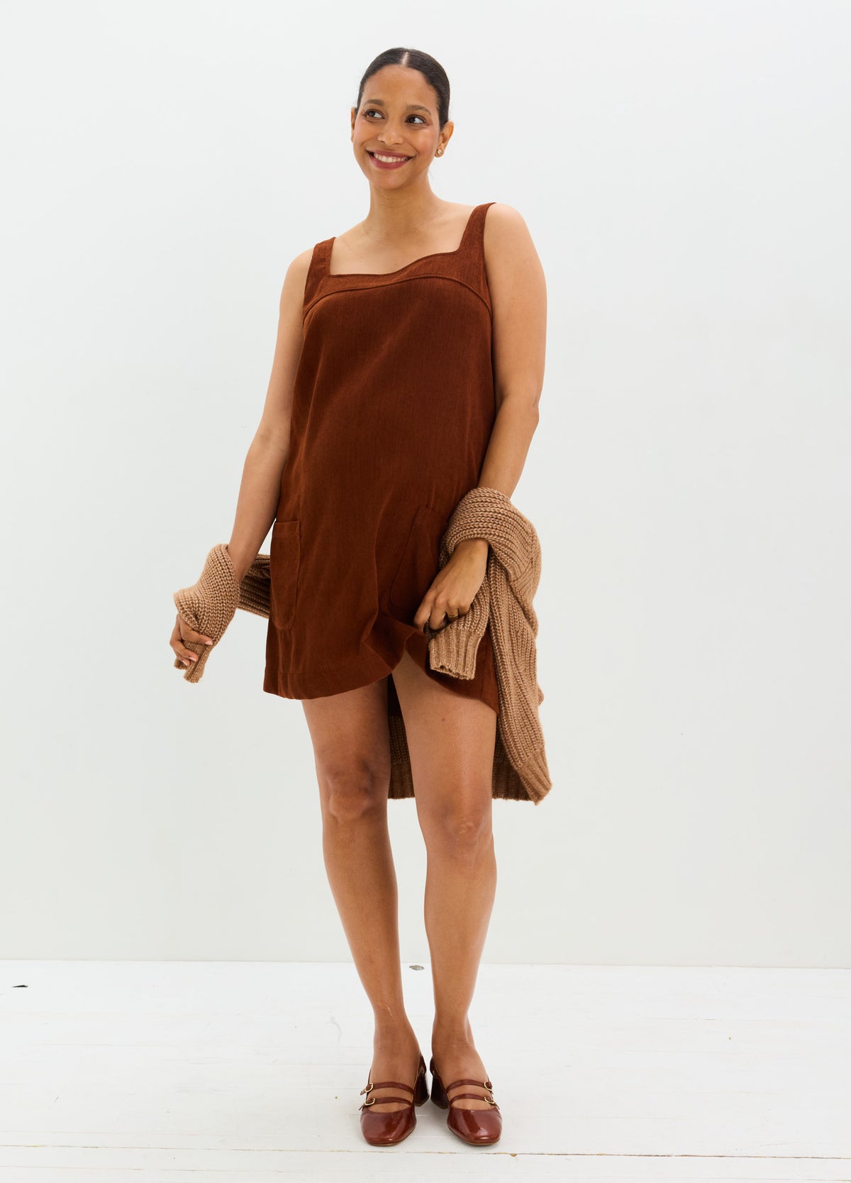 Brown corduroy mini dress with sleeveless design and square neckline, styled for maternity with a relaxed fit, worn by a.