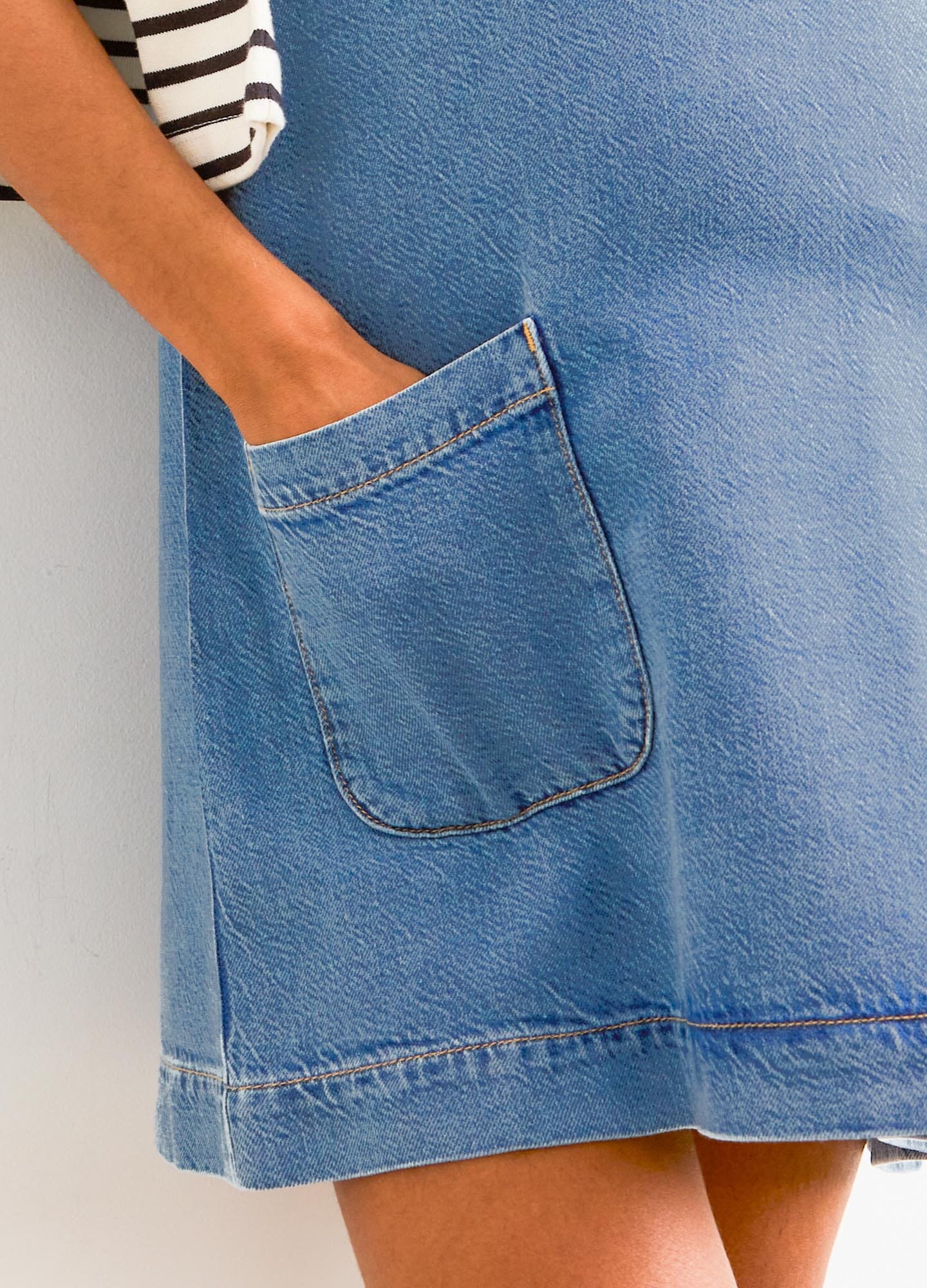 Light blue denim mini dress with front patch pocket and curved hem designed for maternity wear.