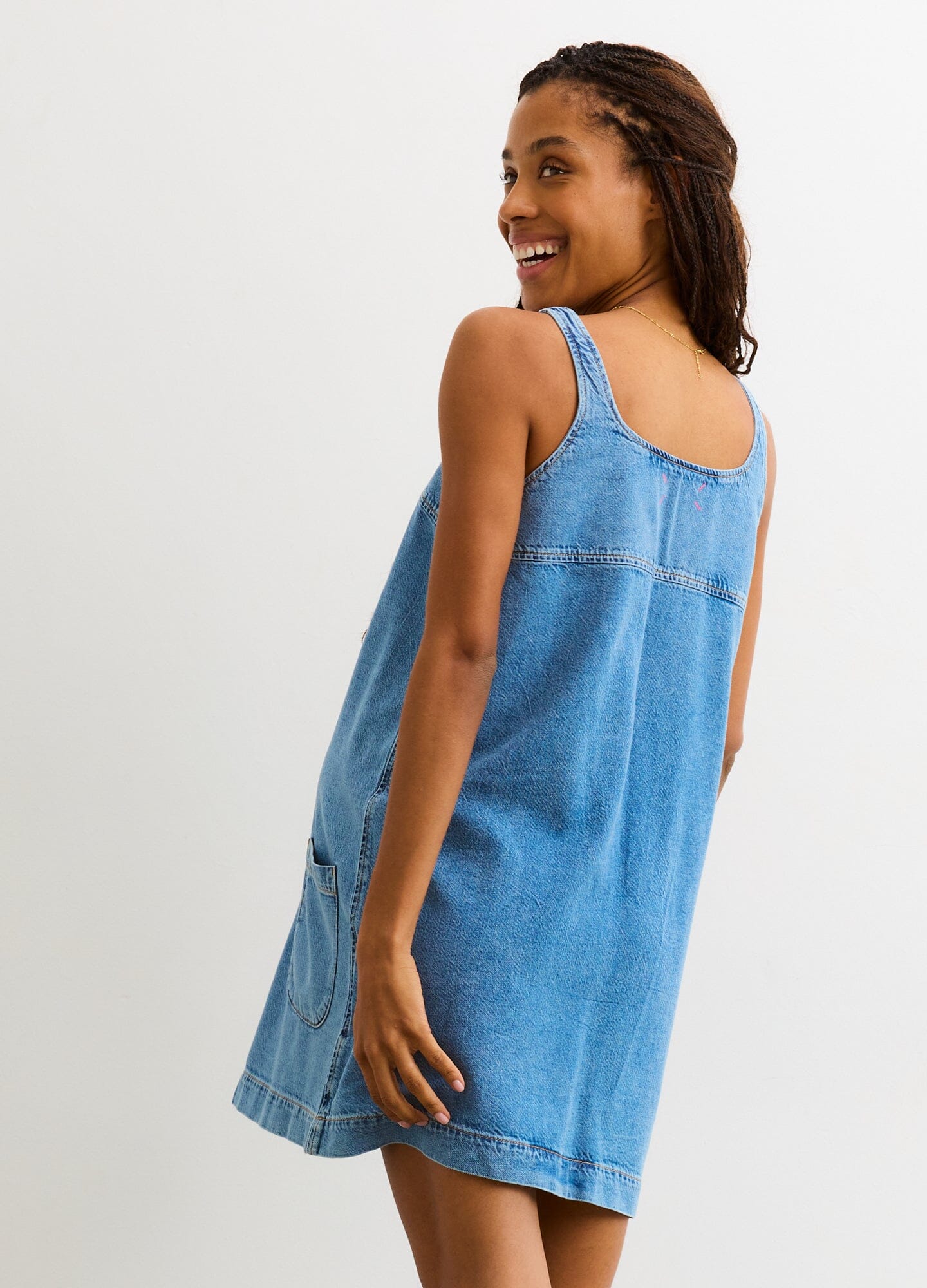 Light blue sleeveless denim mini dress with loose fit designed for maternity wear, modeled from the back.