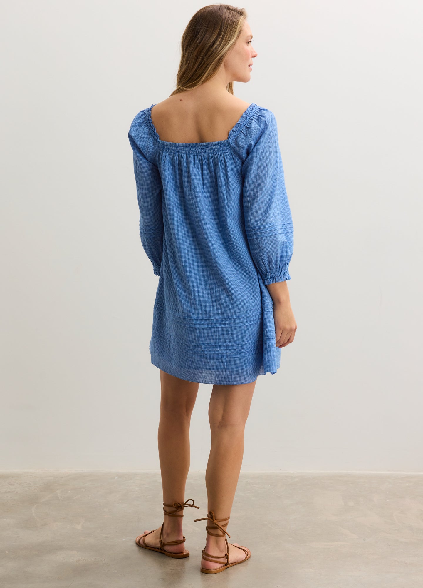 Light blue denim maternity mini dress with long puffed sleeves and square neckline, worn by model from back.