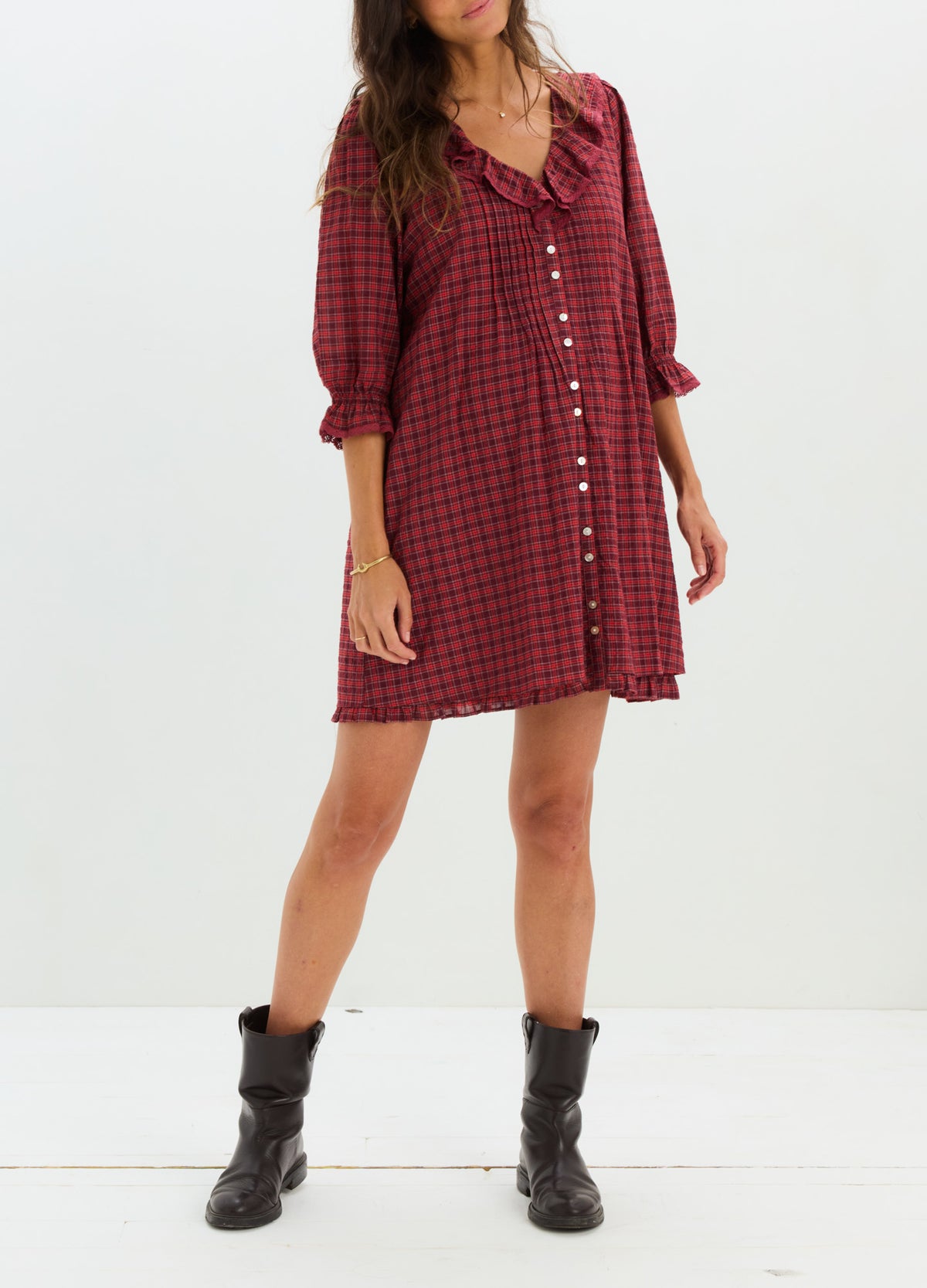 Red and black plaid maternity mini dress with buttons, ruffled neckline, and 3/4 sleeves paired with black ankle boots.