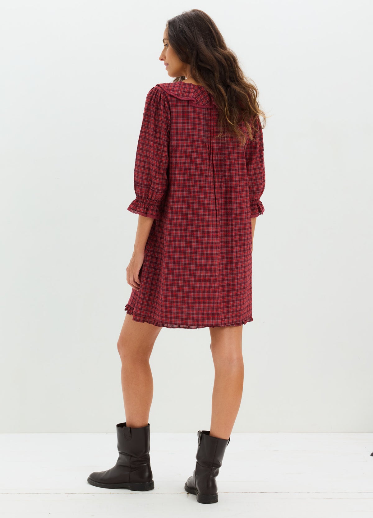 Red and black checkered maternity mini dress with long sleeves and relaxed fit, paired with black ankle boots.