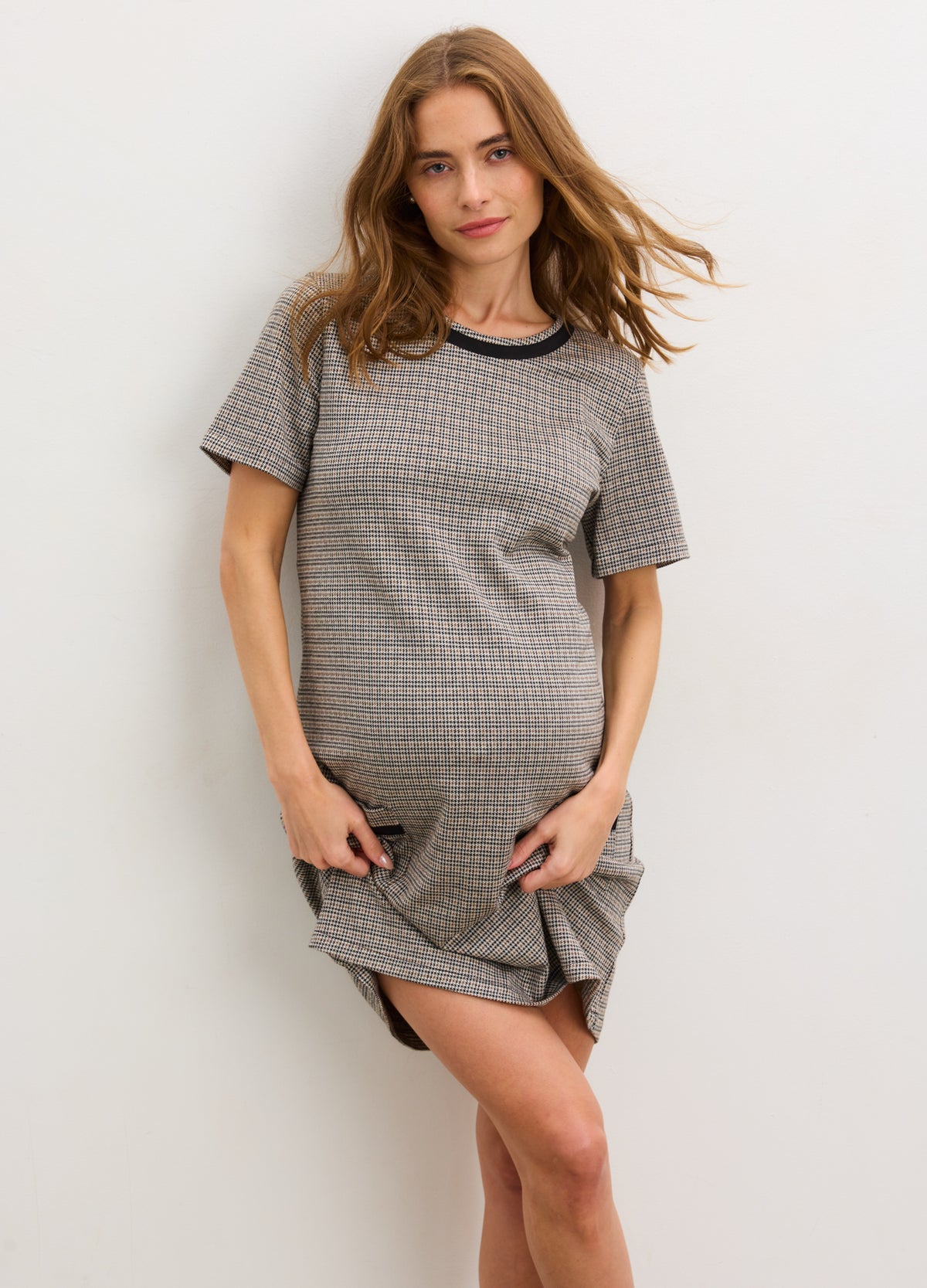Pregnant woman wearing mini houndstooth maternity dress with short sleeves and relaxed fit.