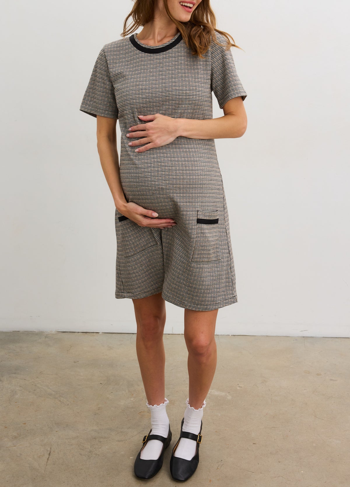 Pregnant woman wearing maternity Louisa Mini Dress in mini houndstooth with short sleeves and front pockets.