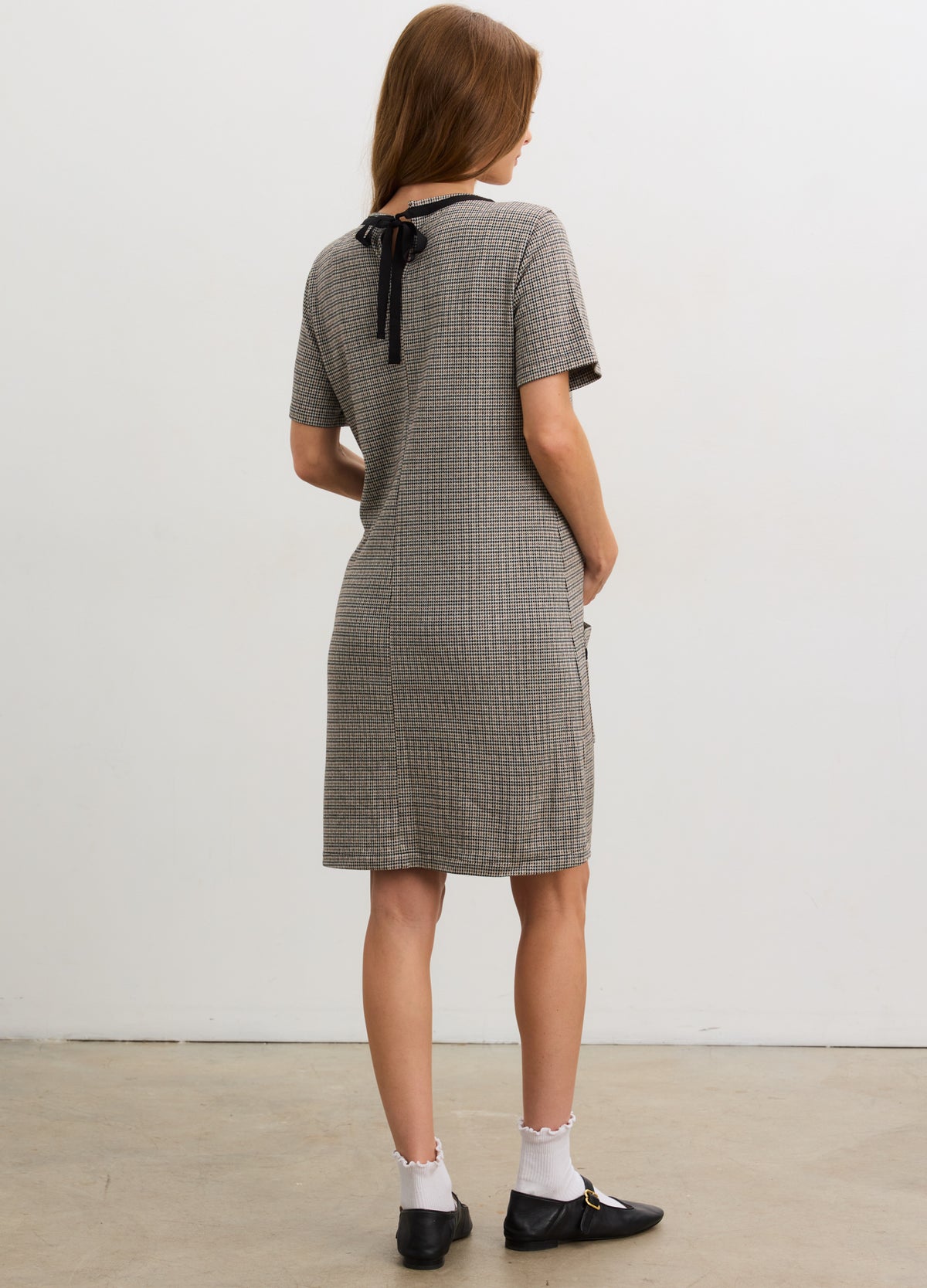Gray and white checkered maternity mini dress with short sleeves and black bow tie at back neckline.
