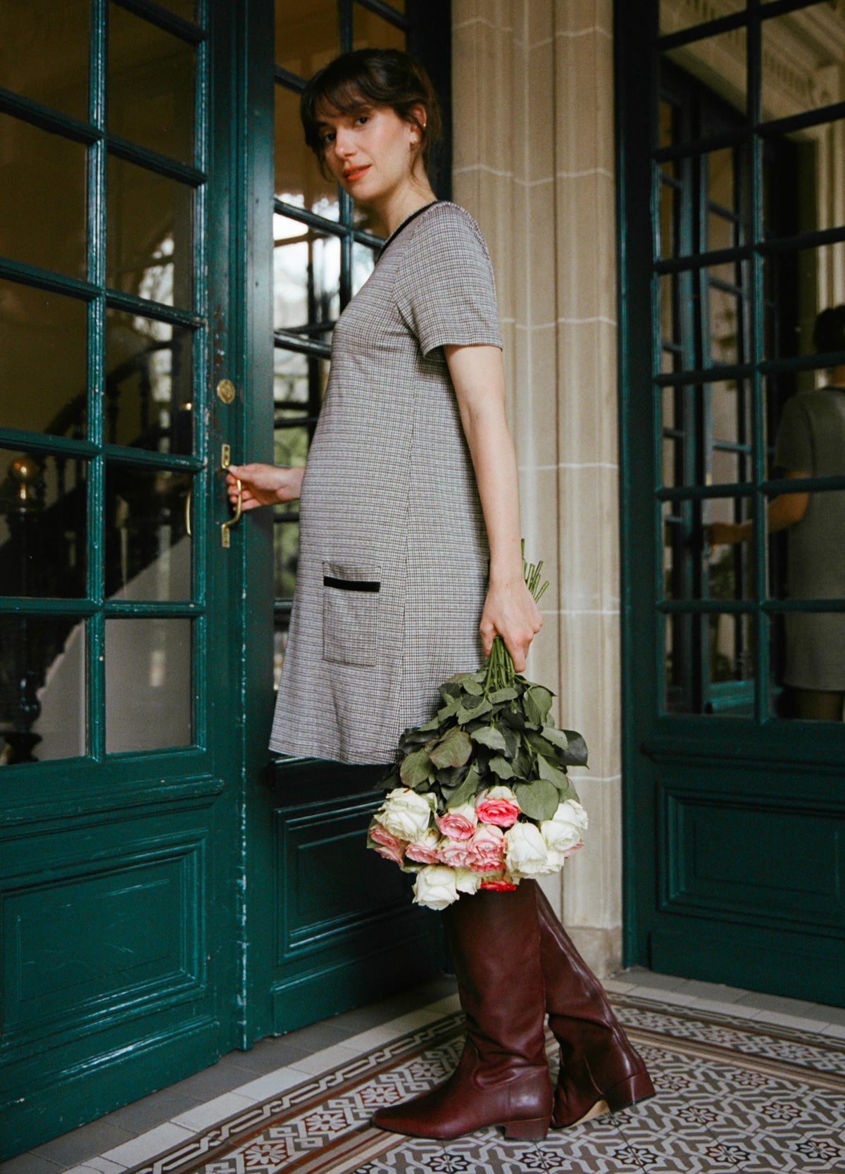 Pregnant woman wearing gray houndstooth maternity mini dress with short sleeves and pockets, holding bouquet.