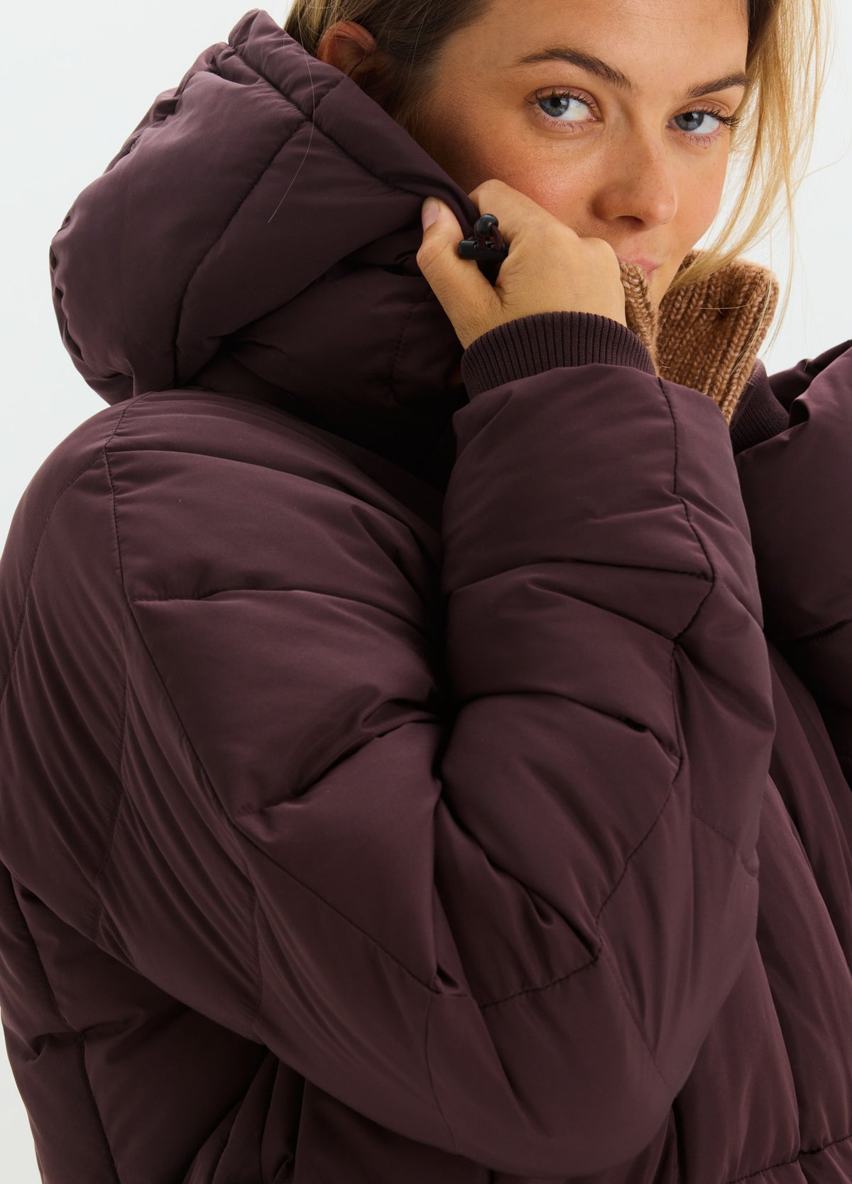 Deep plum puffer jacket with a lofty hood, quilted panels, and a high collar zipped to the chin.