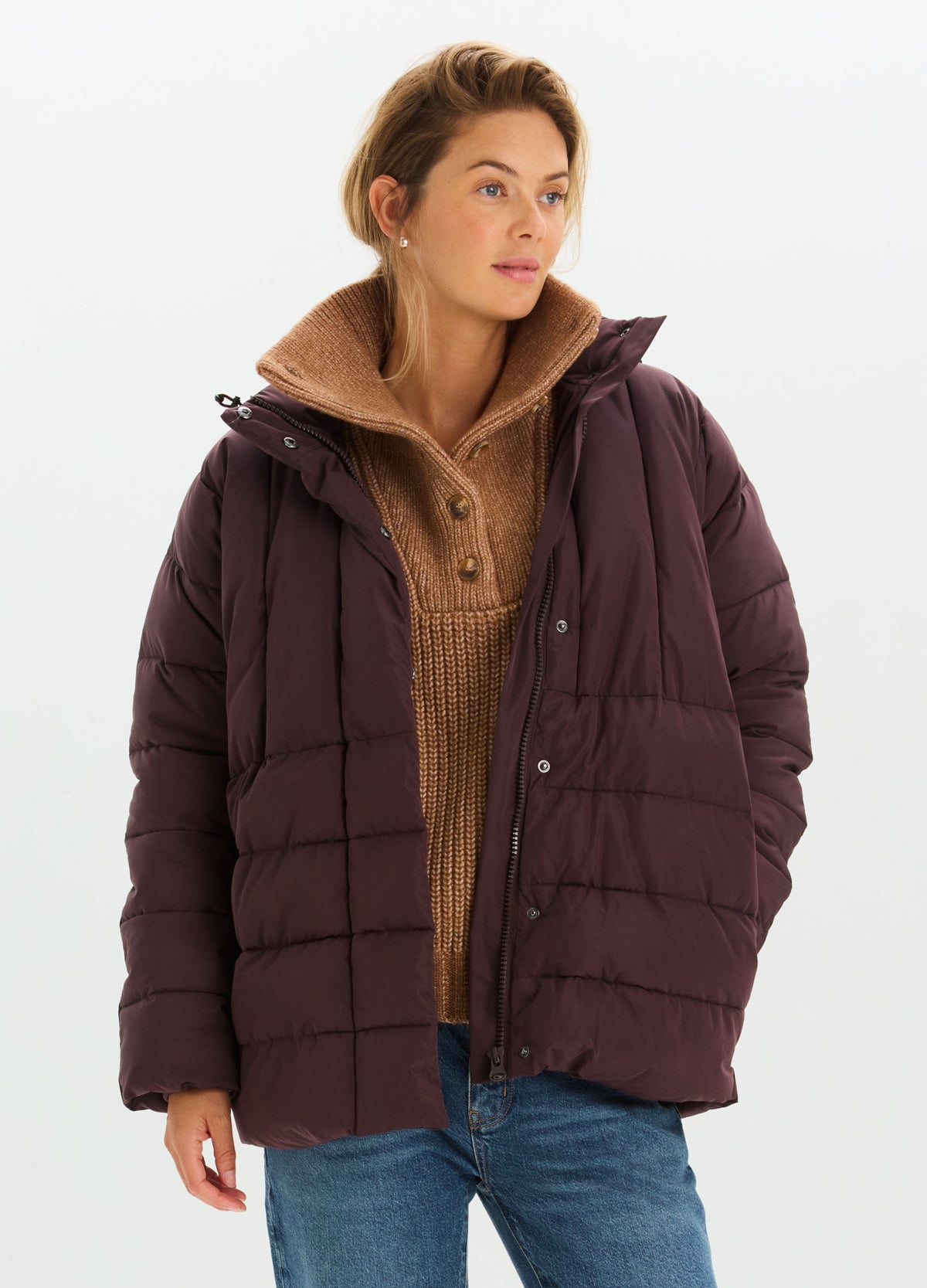Woman wearing a dark plum quilted puffer jacket with a high collar and roomy fit.