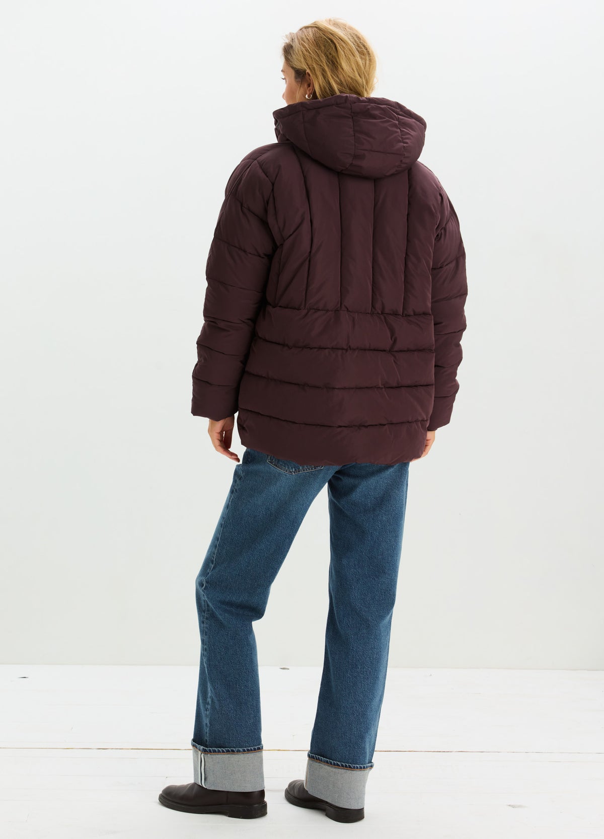 Dark burgundy quilted puffer jacket with a hood, worn with cuffed blue jeans and black shoes.