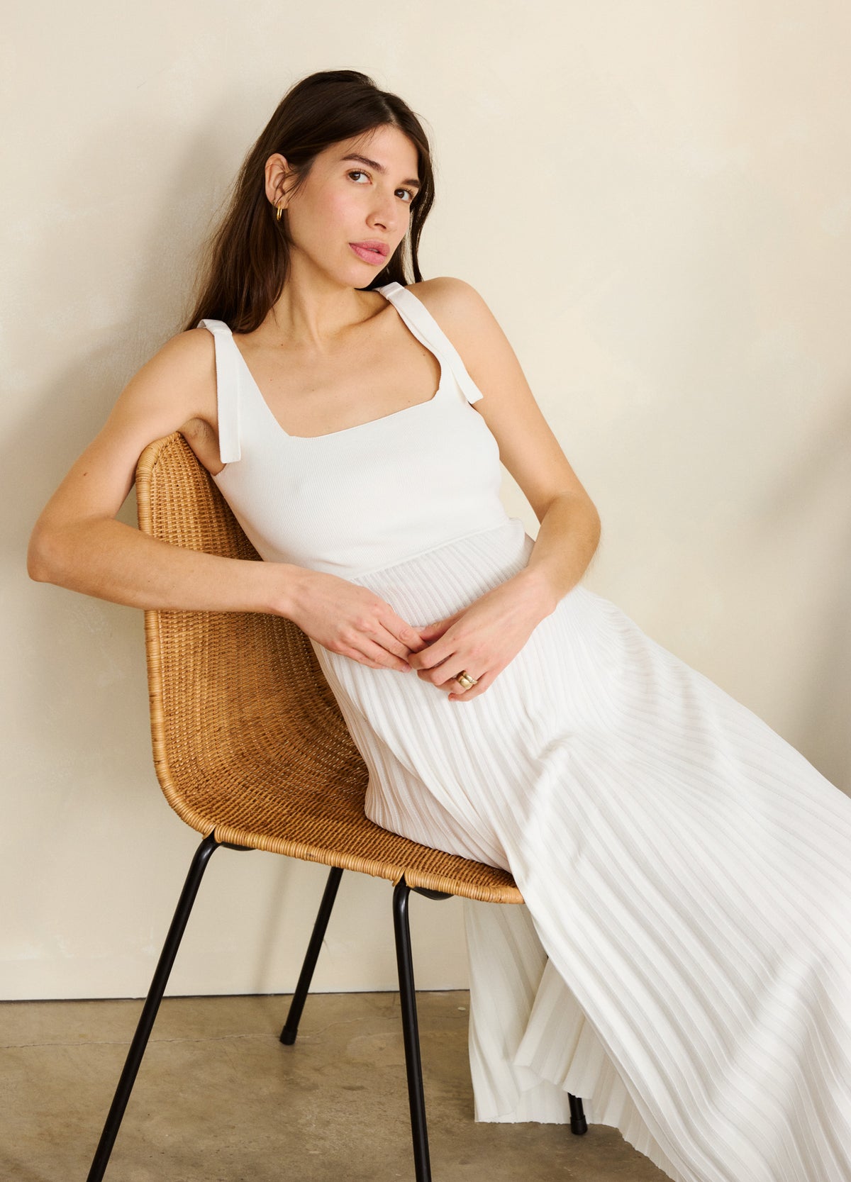 White sleeveless maternity dress with wide straps and a textured, flowy skirt, worn by a seated pregnant woman.