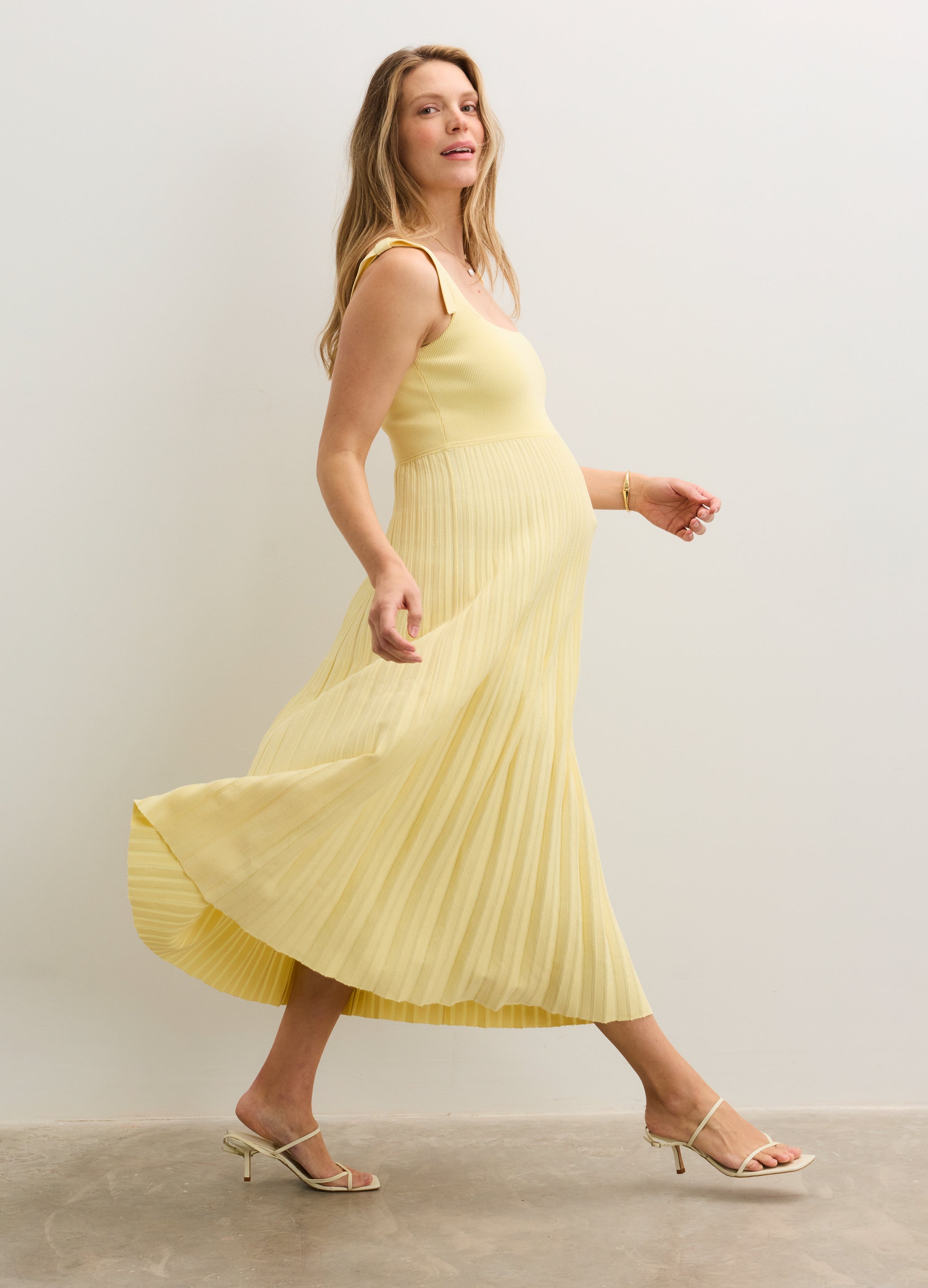 Light yellow sleeveless maternity dress with pleated skirt and fitted bodice, flowy fabric.