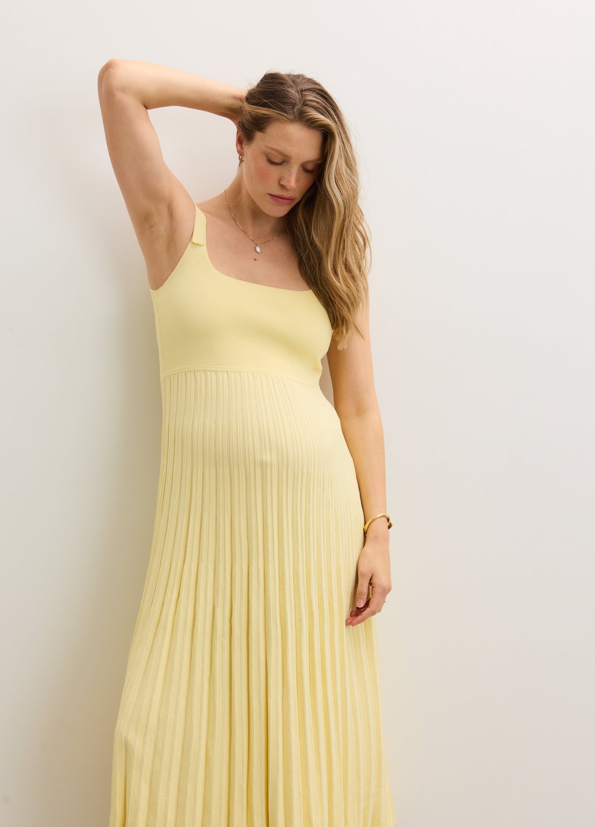 Light yellow sleeveless maternity dress with square neckline and pleated skirt, fitted above belly.