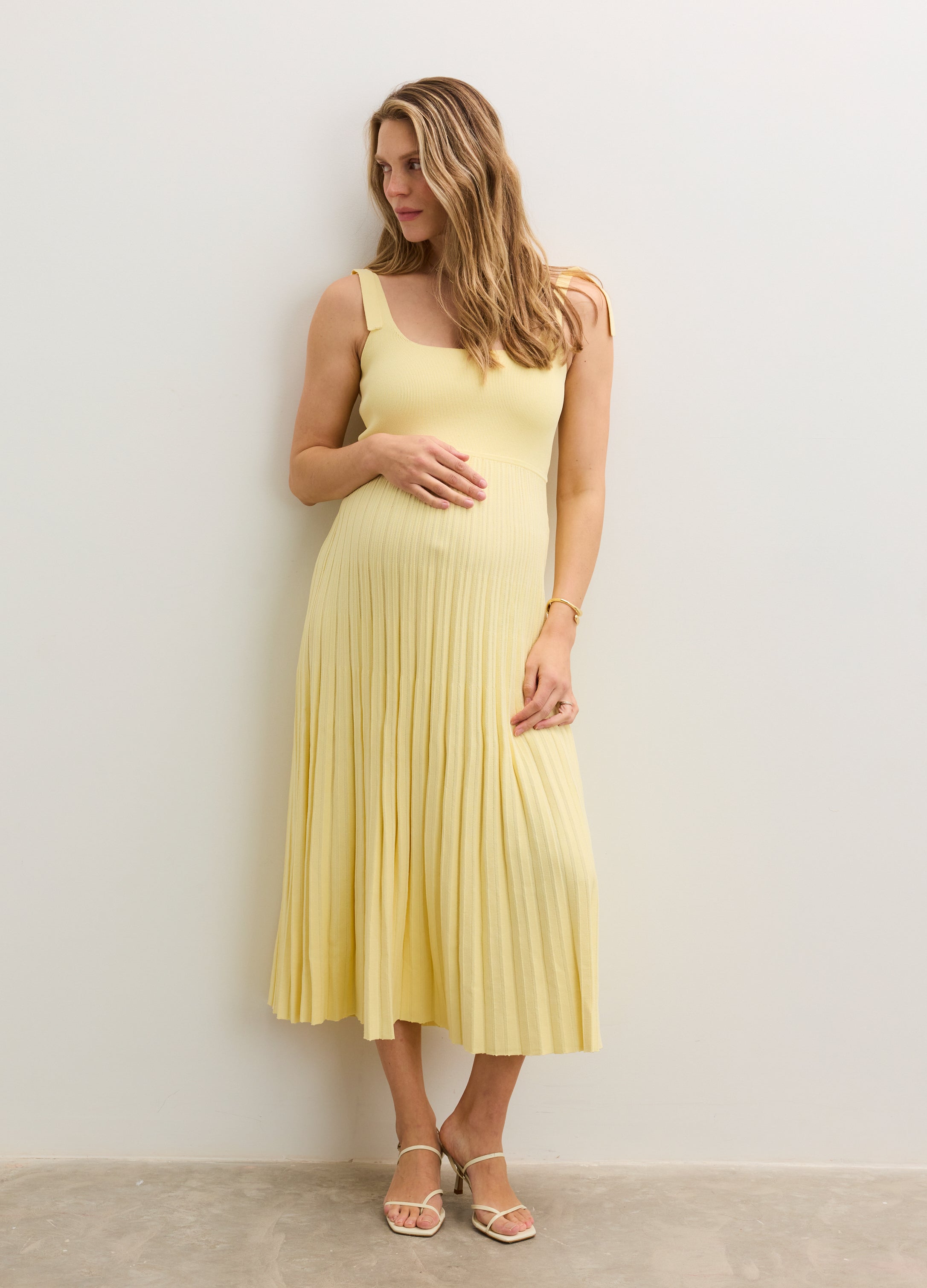 Light yellow sleeveless midi maternity dress with a pleated skirt and a fitted bodice.