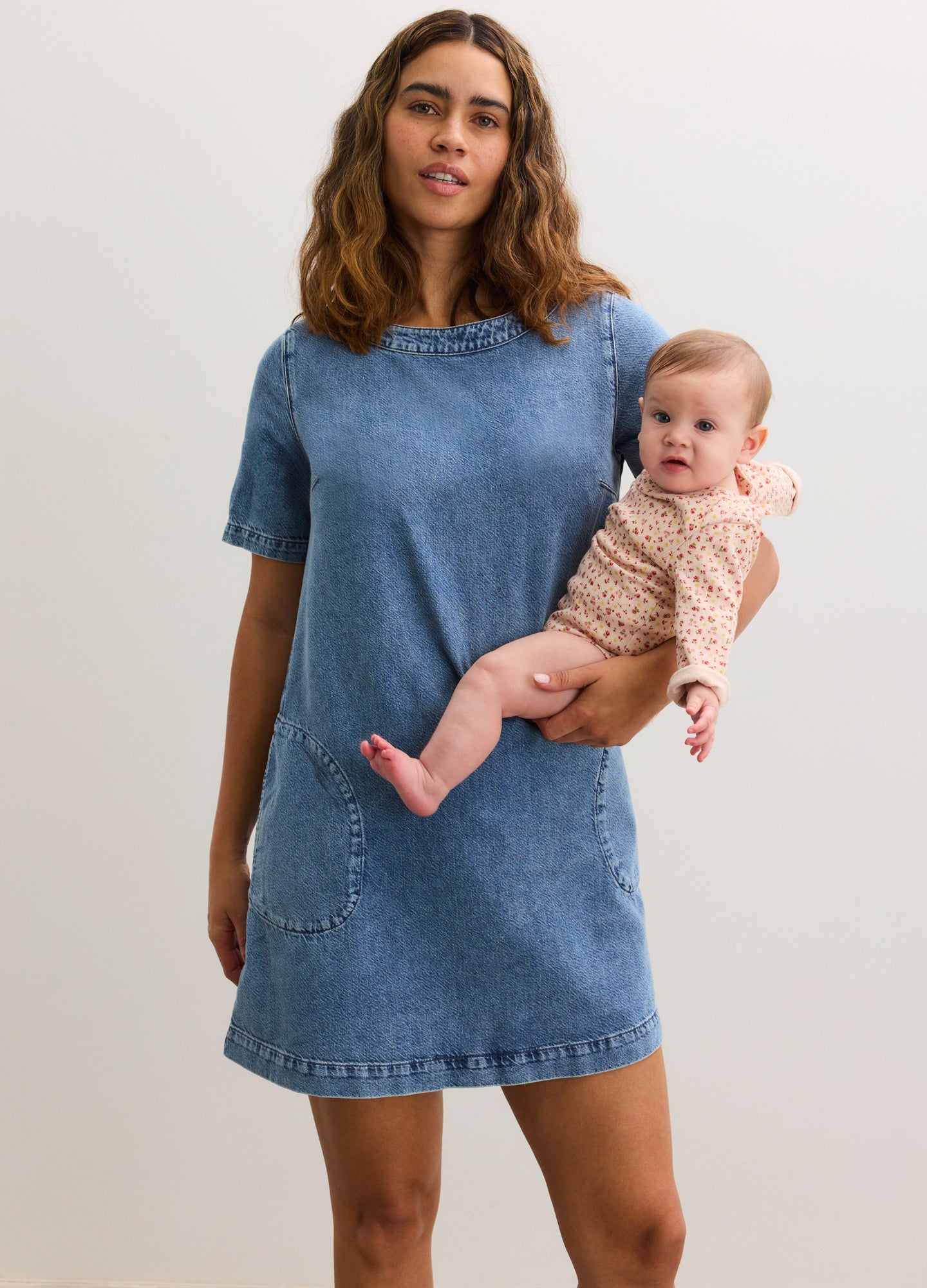 Blue short-sleeve denim maternity dress with distressed details, worn by pregnant model holding baby.