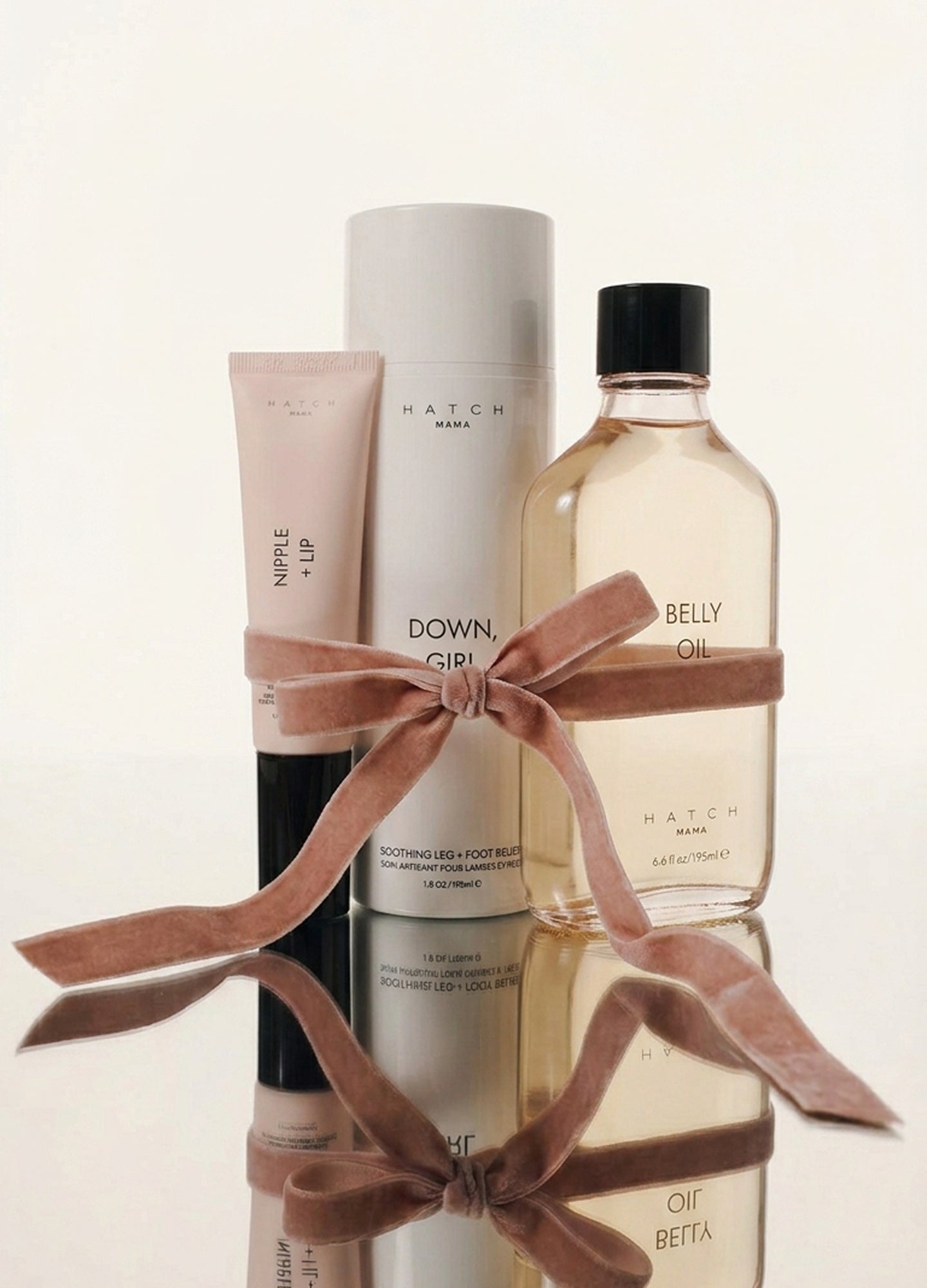 Mama Must-Haves Kit with blush pink lotion tube, tall white cylindrical container, and clear bottle with beige liquid, tied.