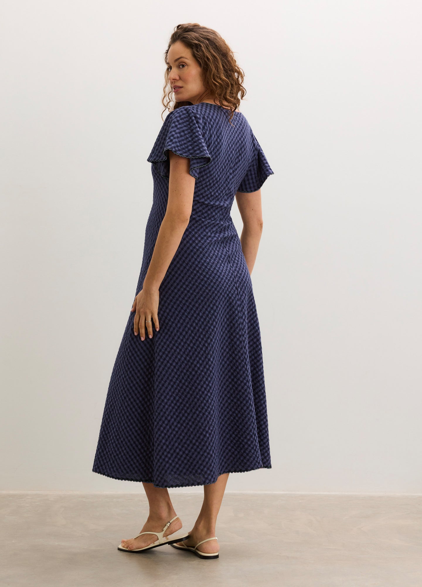 Navy blue maternity dress with short flutter sleeves and a fitted waist, midi length, textured fabric.
