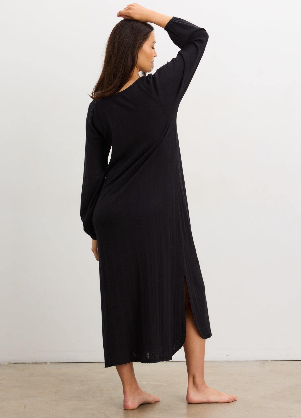 Black long sleeve pointelle knit nightgown with mid-calf length and side slit, worn by a standing woman.