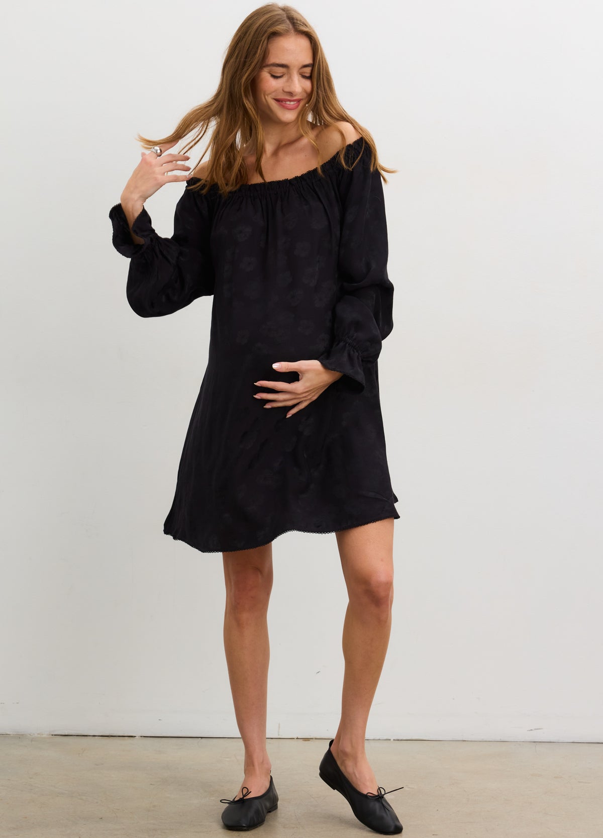 Black off-the-shoulder jacquard mini dress with long sleeves, loose fit for maternity, worn by pregnant model.