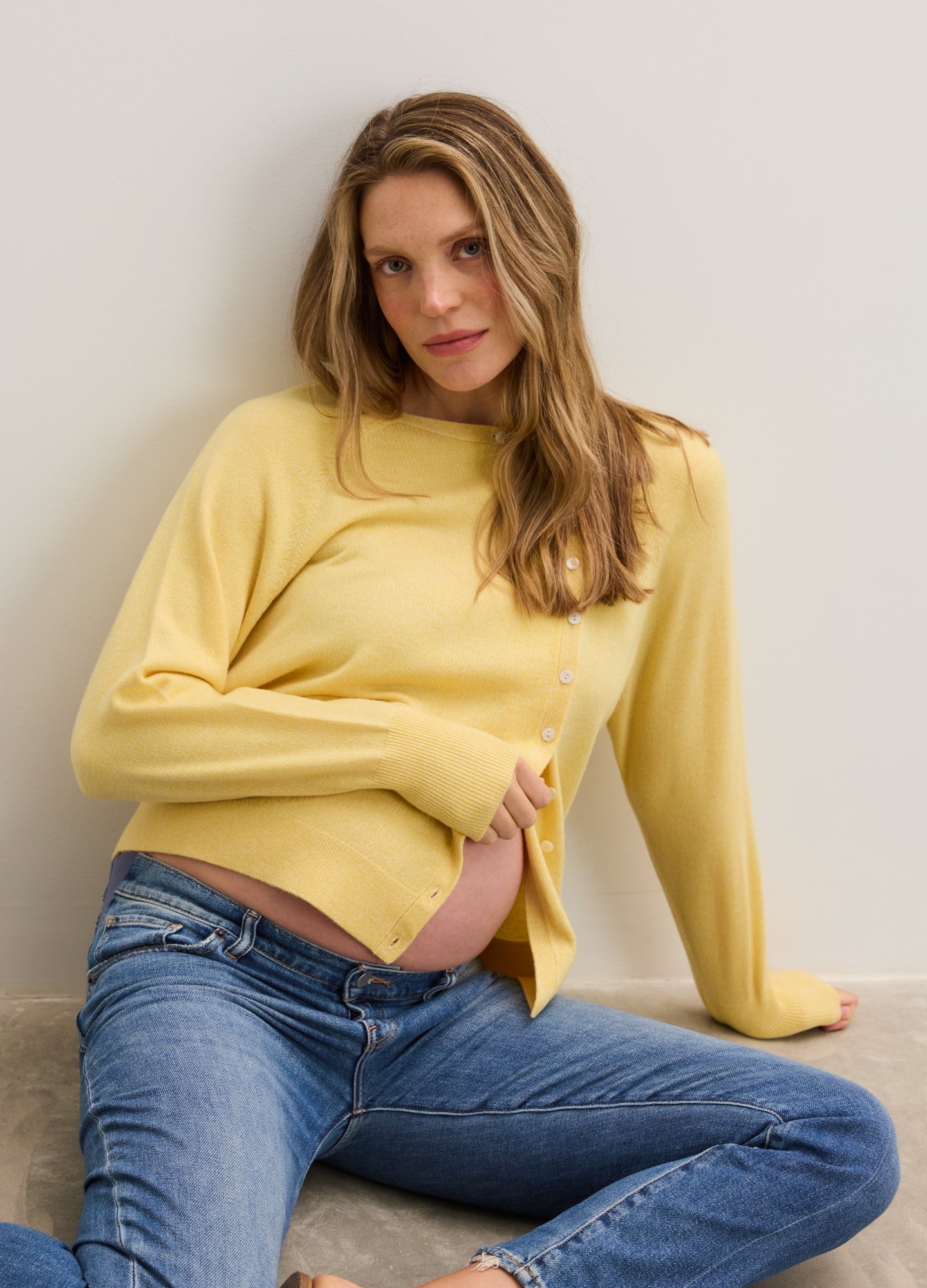 Soft yellow maternity cardigan with side slits, worn open over baby bump, paired with blue jeans.