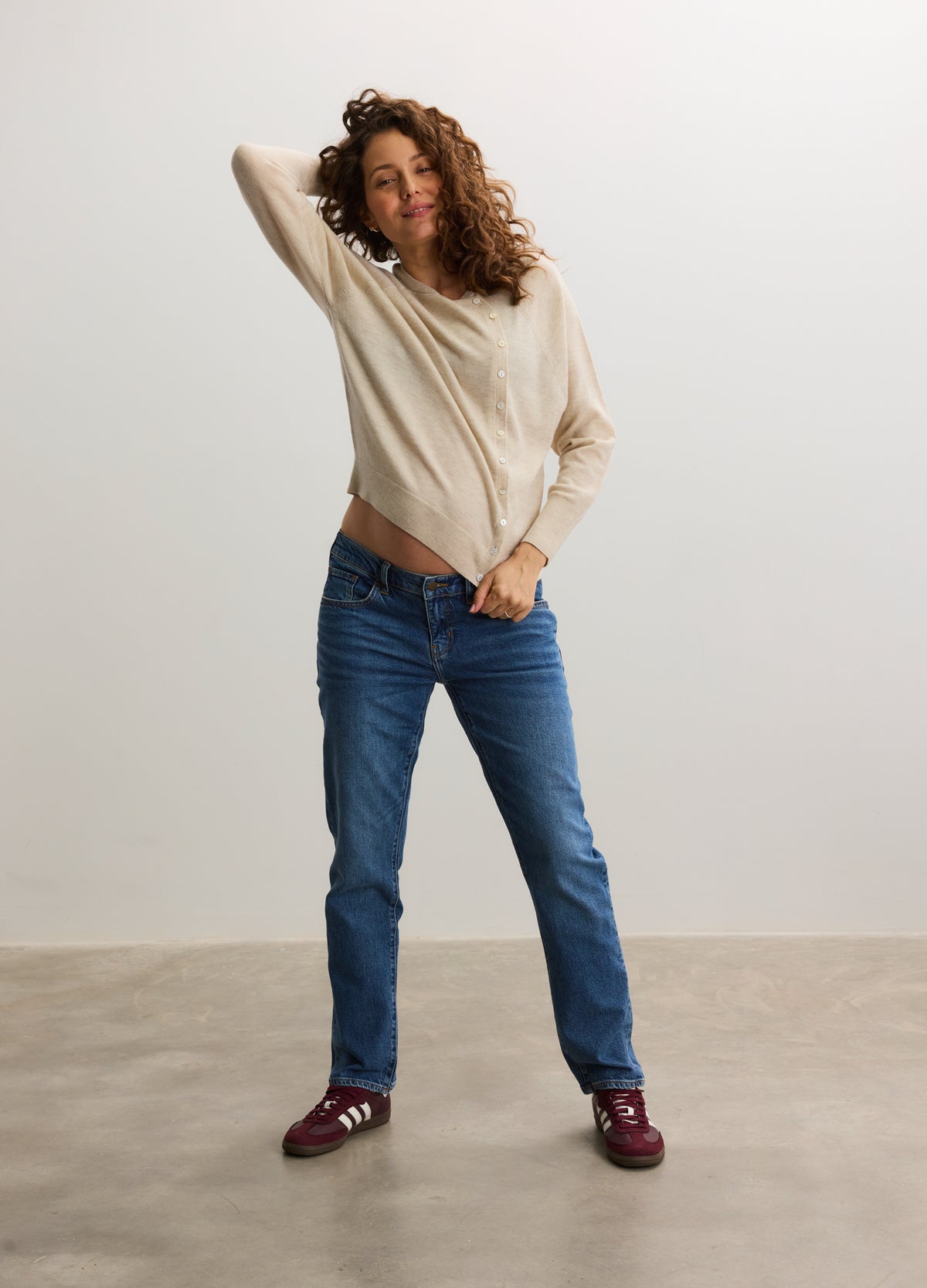 Beige maternity cardigan with long sleeves and relaxed fit, paired with dark blue jeans and burgundy shoes.