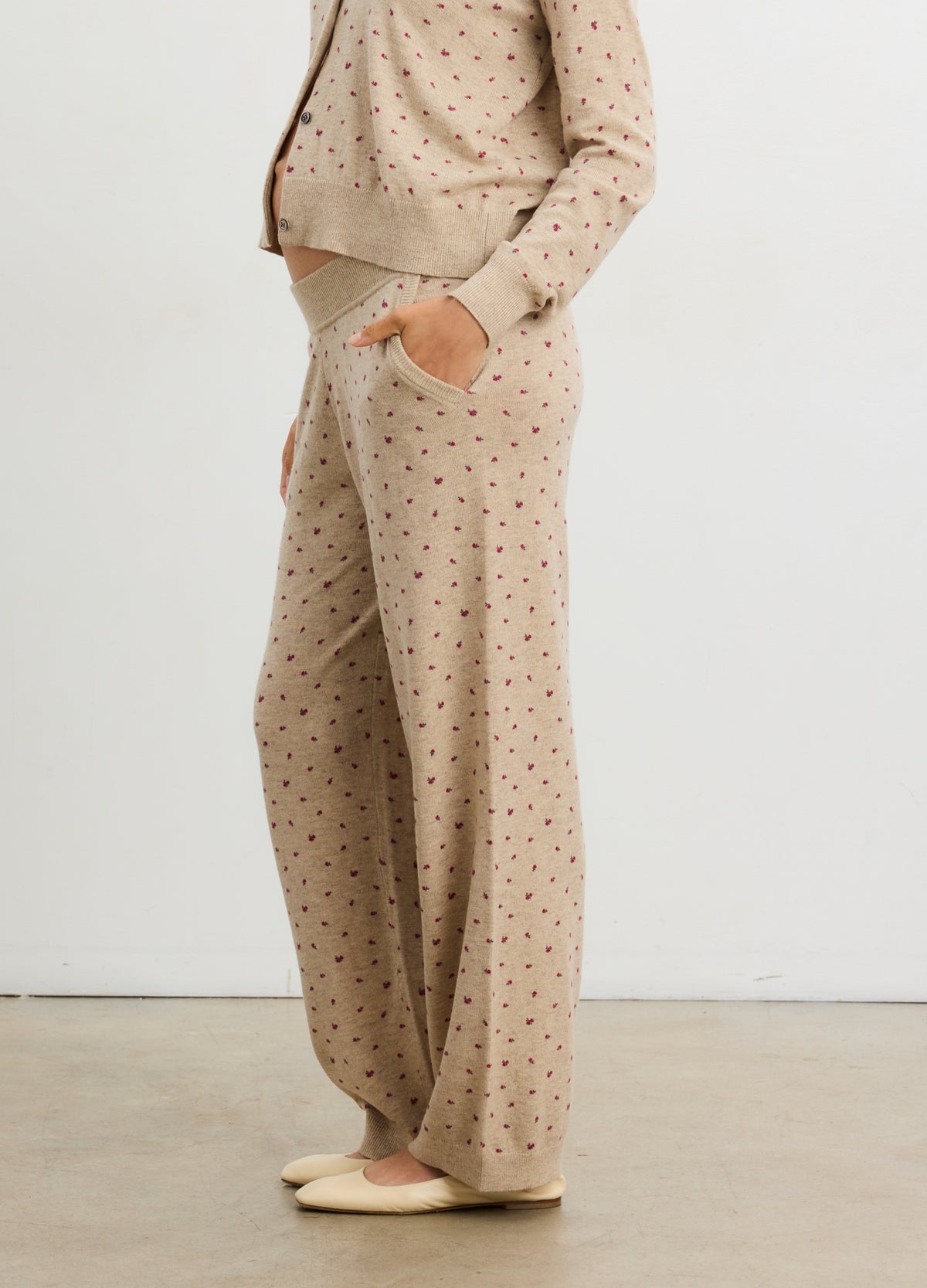 Beige maternity knit pants with small red floral print, stretchy waistband, side pockets, and relaxed fit.