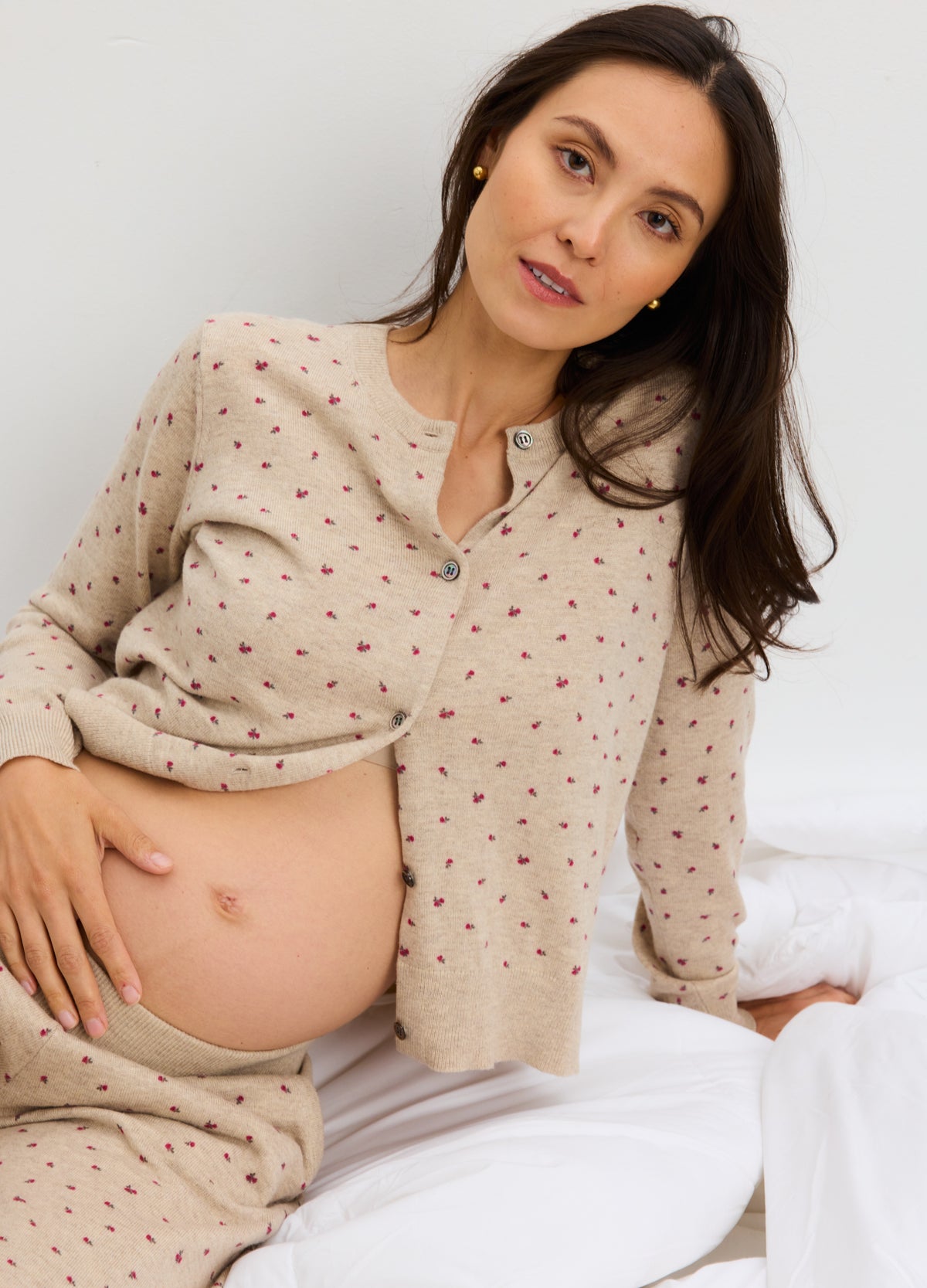 Beige knit maternity cardigan with small red floral pattern, worn open over pregnant belly.