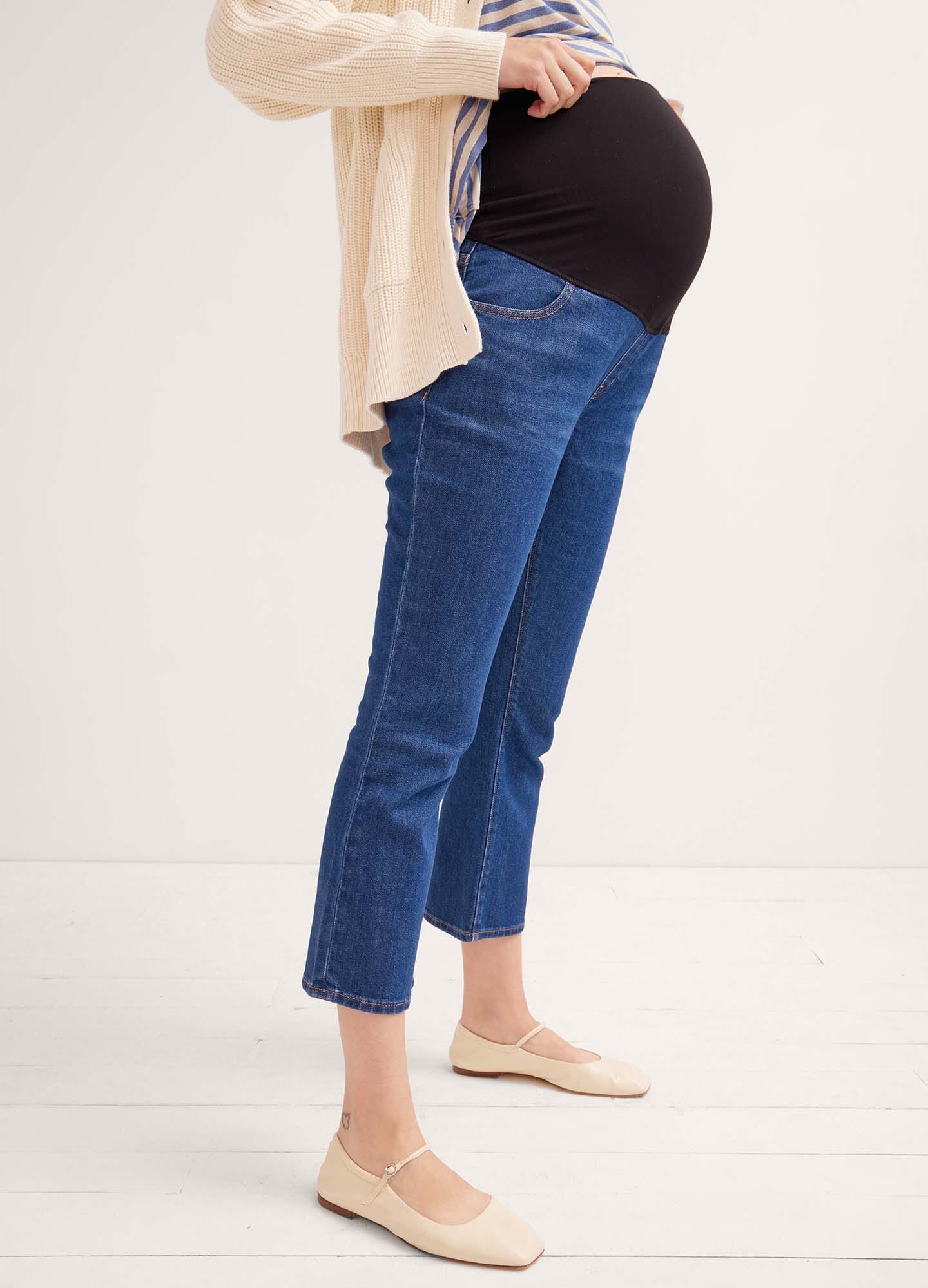 Dark blue cropped maternity jeans with an over-the-bump stretchy waistband, worn with beige flats and a cream cardigan.