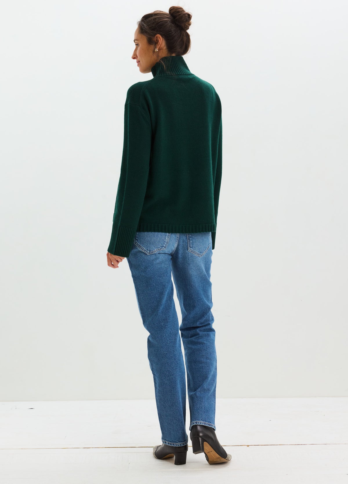 Pregnant woman wearing light blue straight maternity jeans with an over-the-bump waistband and a dark green turtleneck.