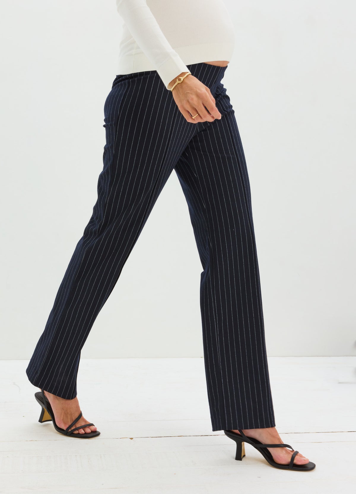 Navy pinstripe maternity work pants with seamed detailing, fitted through the leg, paired with black open-toe heels.