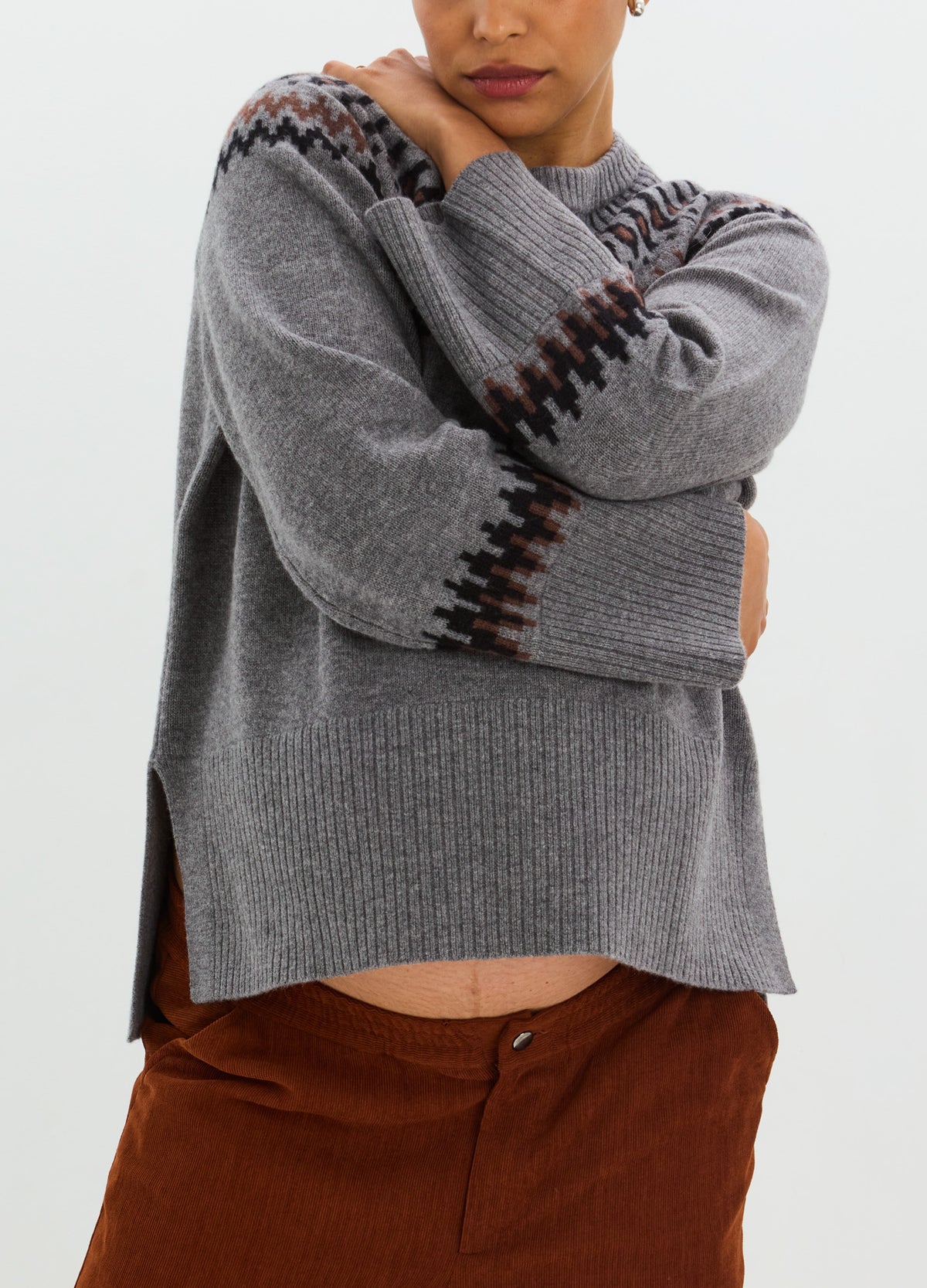 Gray knit Fairisle sweater with dark geometric bands, a relaxed fit, and side slits.