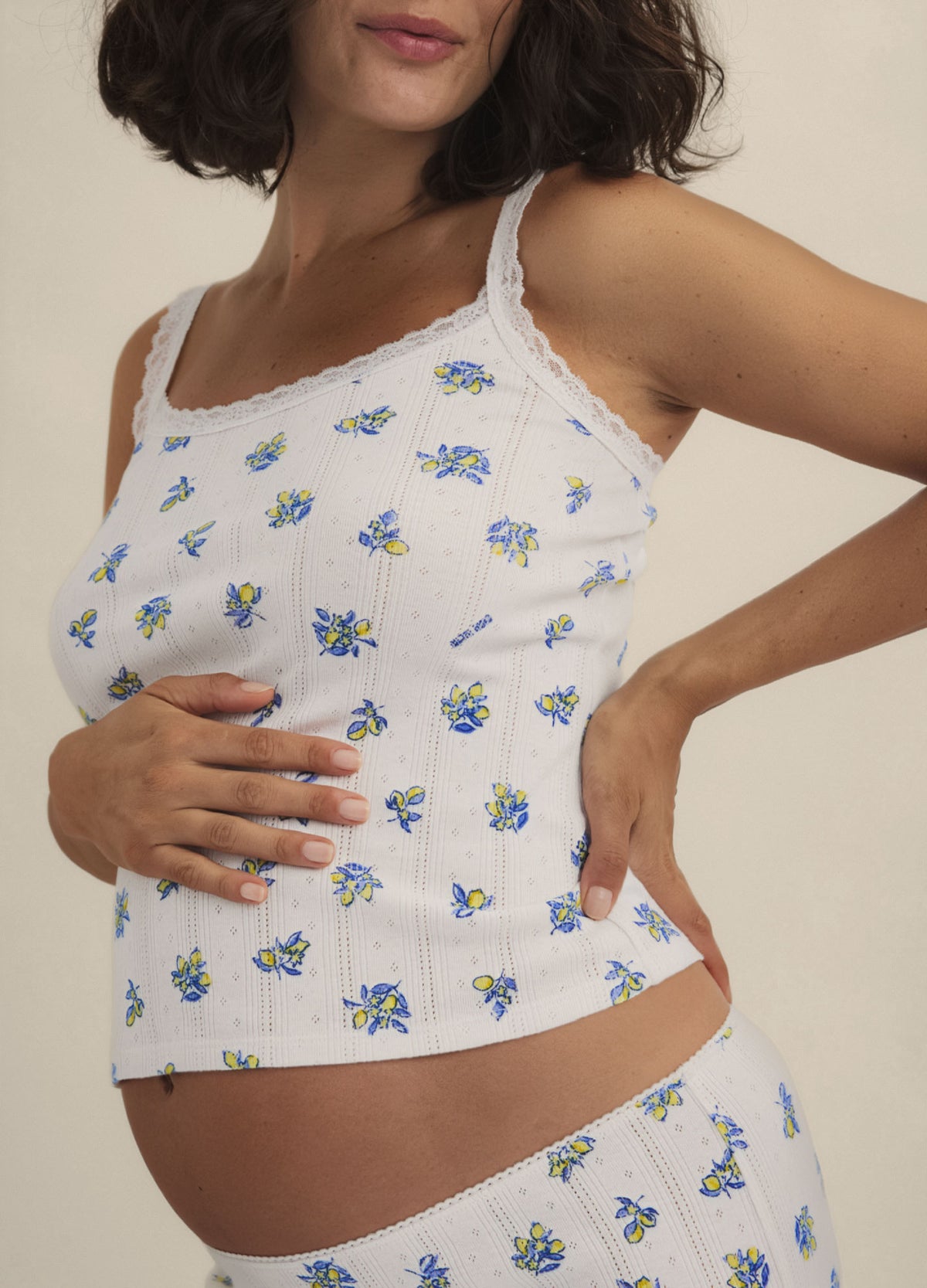 White ribbed maternity cami with blue and yellow floral print, delicate lace trim, and thin straps.