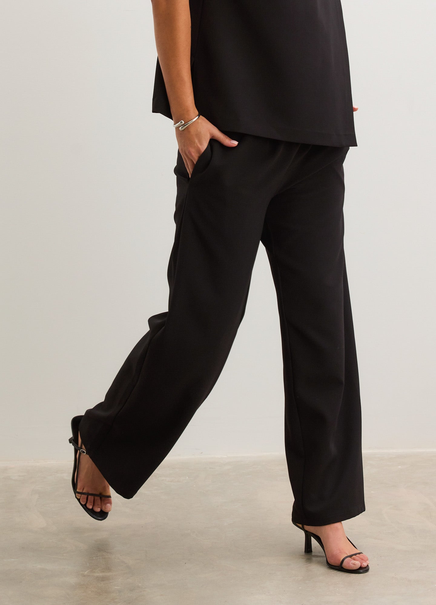 Black straight-leg maternity pants with a smooth elastic waistband, styled with black sleeveless top and heels.