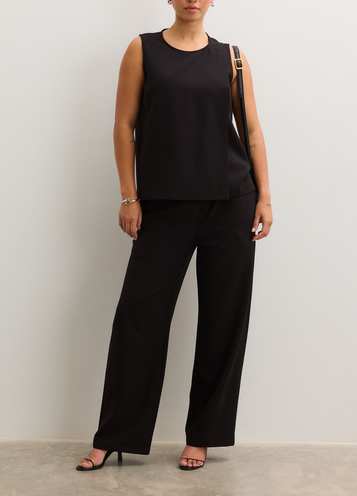 Black sleeveless nursing tank with a round neckline, paired with loose black maternity pants.