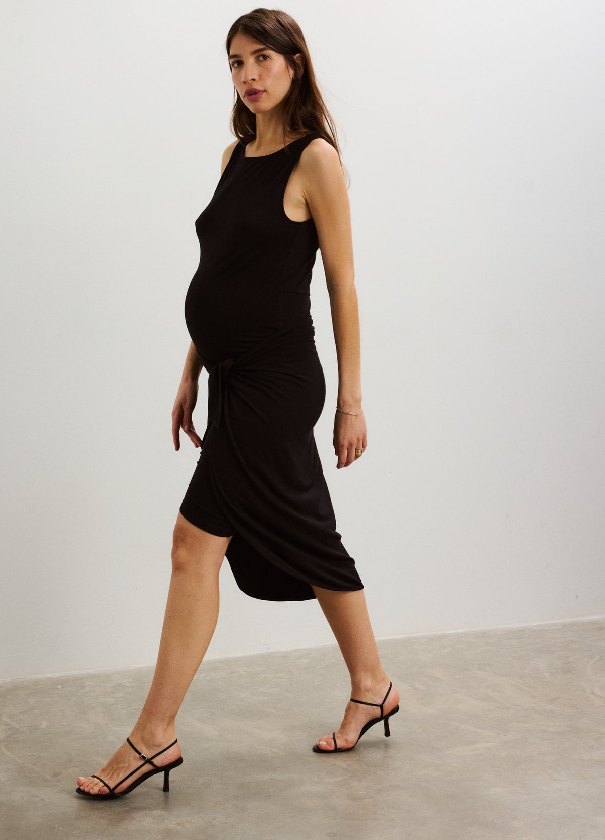 Black sleeveless maternity wrap dress with knee-length hem and fitted silhouette, styled with strappy heels.