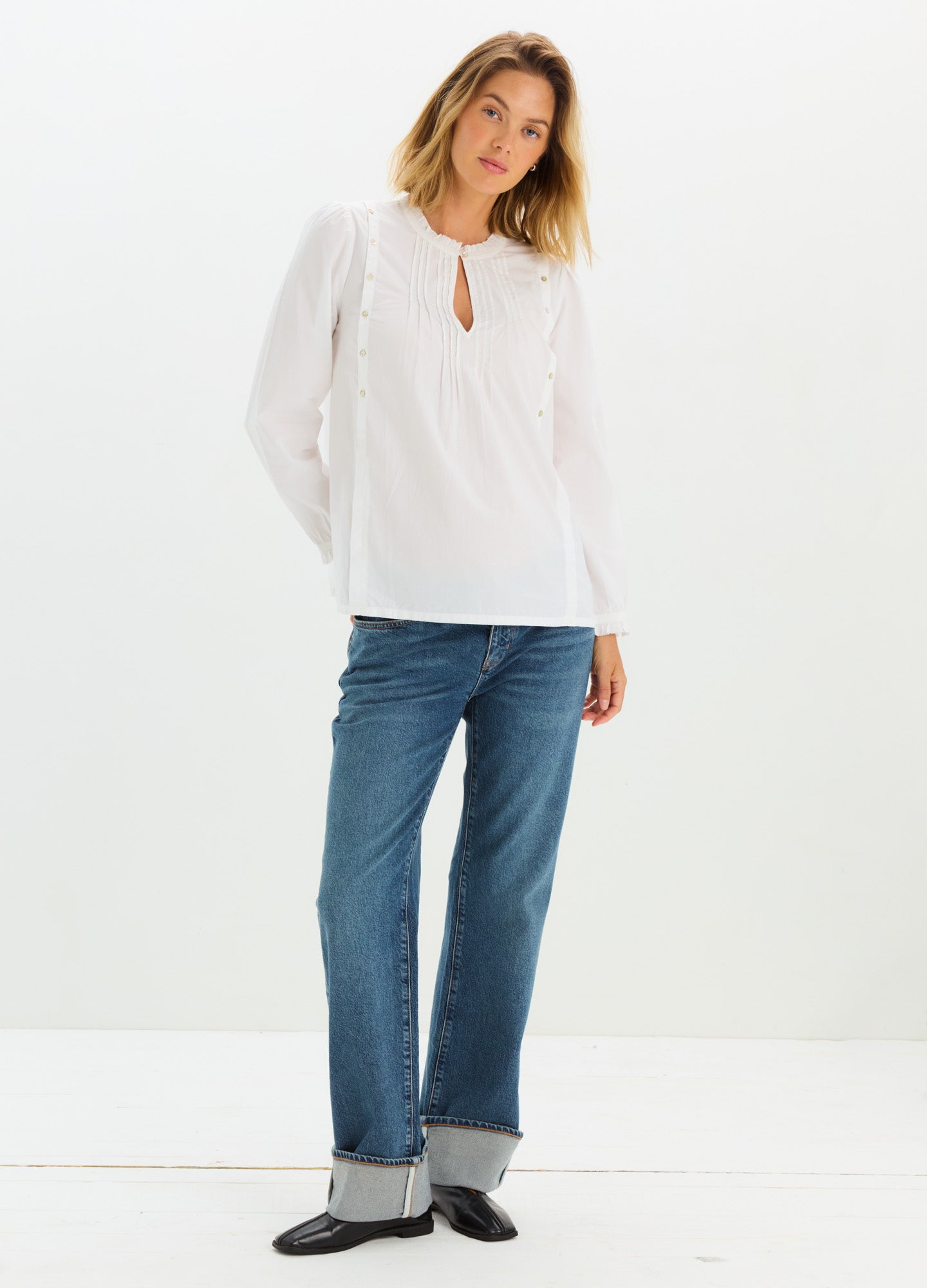 Blue relaxed-fit maternity jeans with cuffed hems, styled for pregnant women, paired with a white blouse.