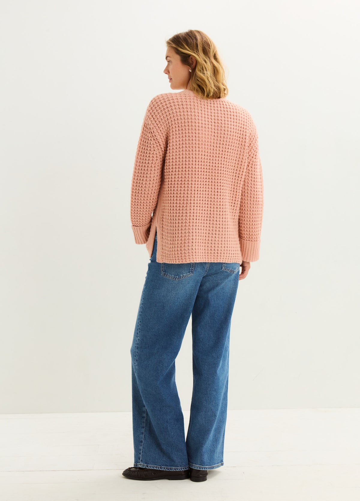 Pregnant model wearing relaxed blue wide-leg maternity jeans with a stretchy belly panel and a peach knit sweater.