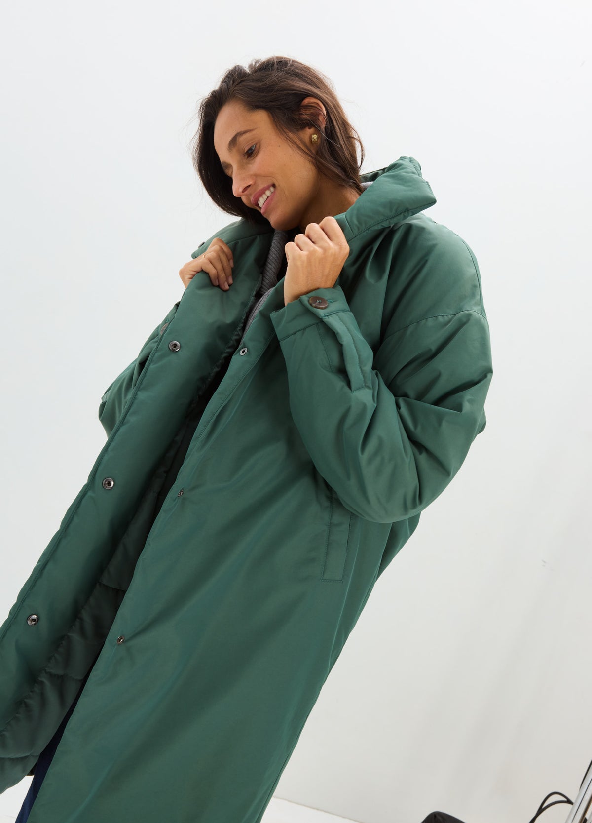 Woman wearing a long teal puffer coat with a hood, quilted panels, and snap-button closure.