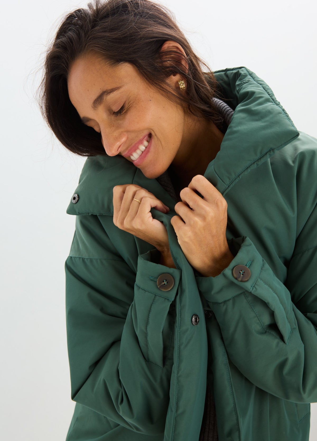 Woman wearing a deep green padded coat with a high collar, snap-button front, and cozy quilted sleeves.
