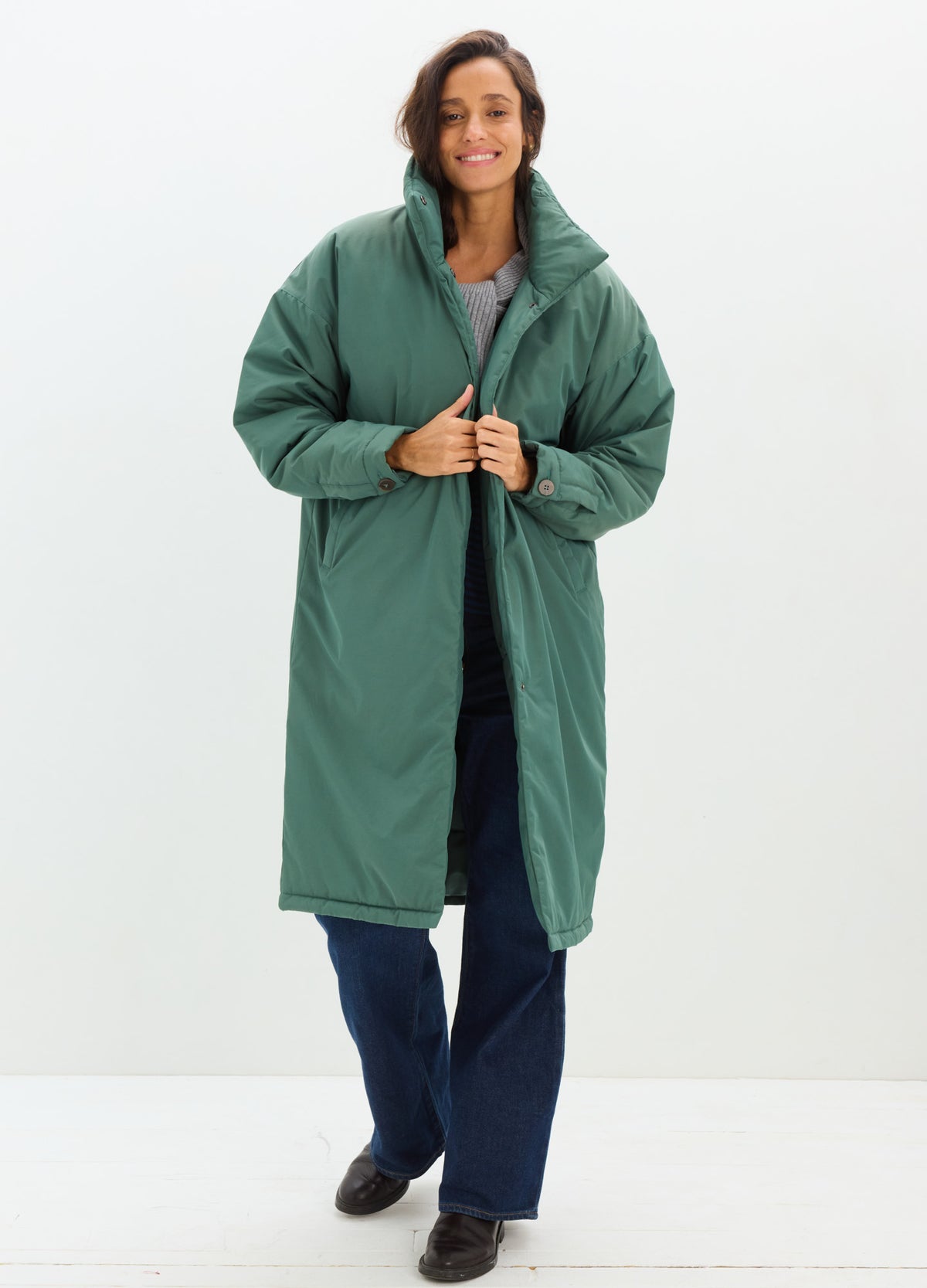 Long teal-green padded coat with a quilted finish, oversized sleeves, and a front snap closure.